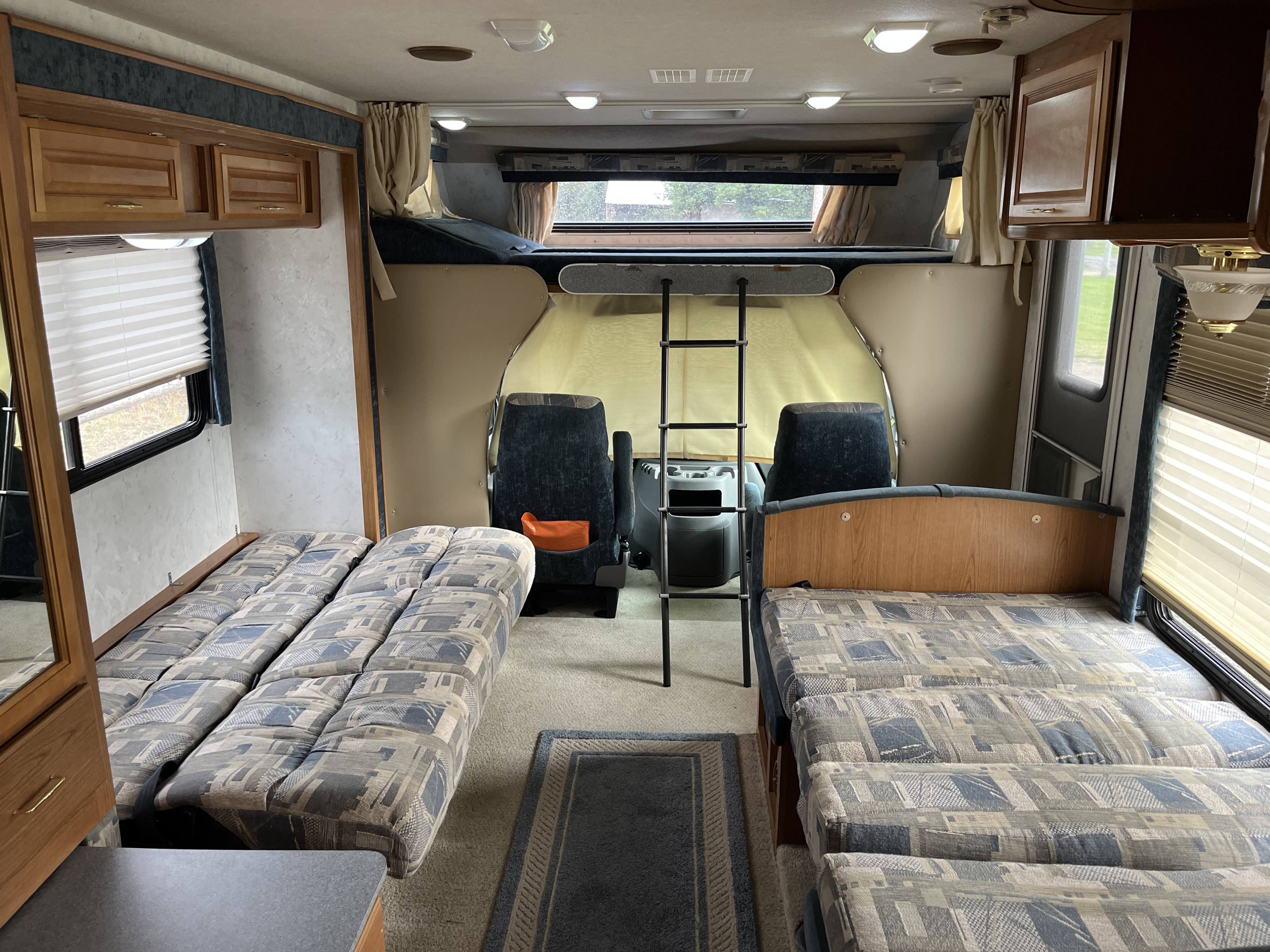 Inside this RV rental, dual patterned sofa-beds, front cockpit area, and overhead bunk create a functional living space.. Tioga Tioga Motorhome 2001