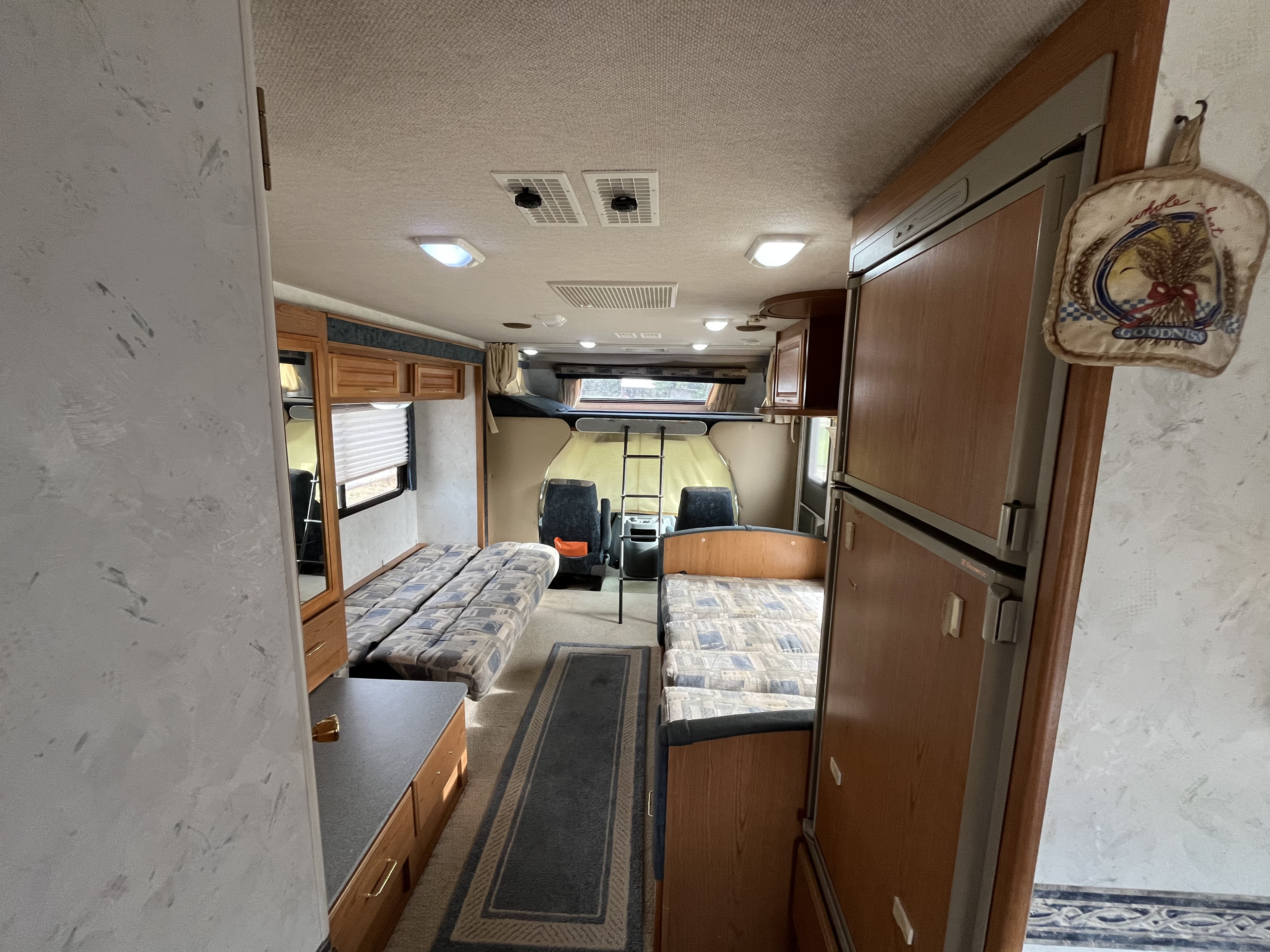 Interior of an RV rental: features beds, a large fridge, overhead bunk, and driver's area, offering ample living space.. Tioga Tioga Motorhome 2001