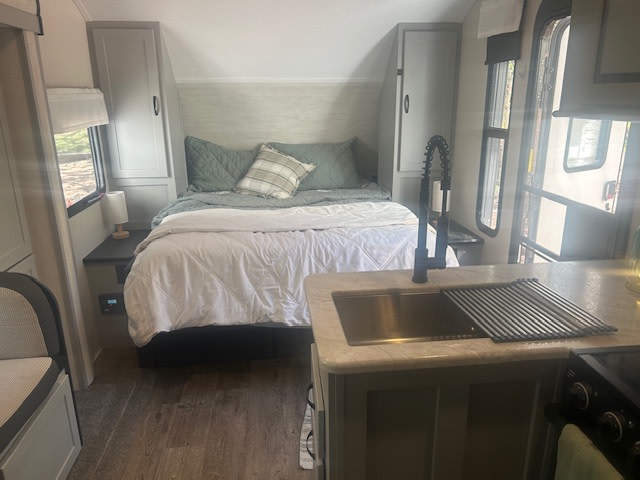 Cozy RV rental interior: bedroom with bed, cabinets, and kitchen area with sink & counter.. Forest River Vibe 2021