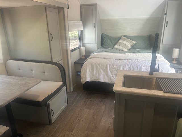 Cozy RV rental interior: bedroom with bed, dining booth, & kitchen sink. Ideal for comfortable travel.. Forest River Vibe 2021