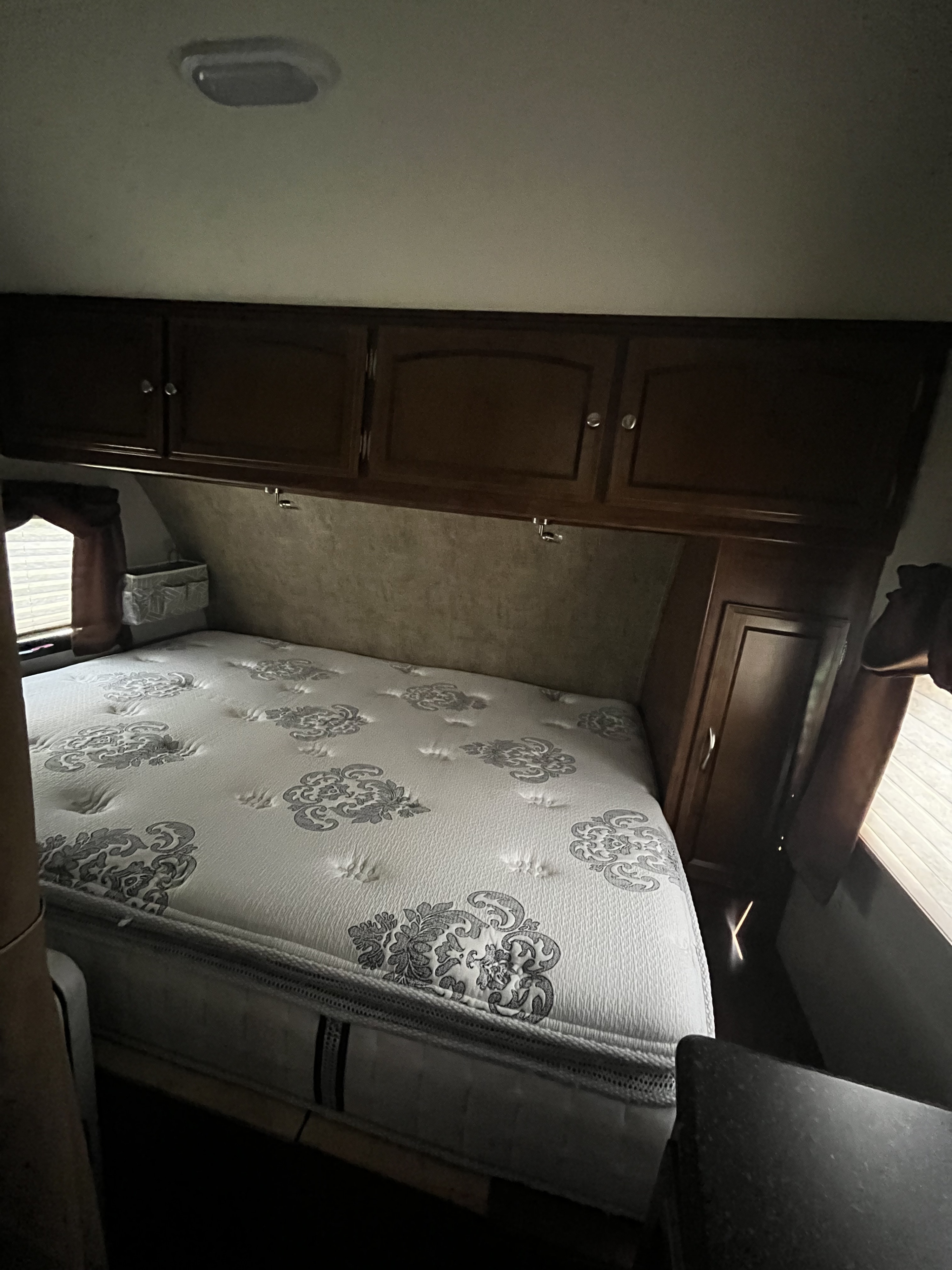 RV rental bedroom with patterned mattress, overhead storage cabinets, and side window, offering a compact, comfortable space.. Coachmen Freedom Express 2017