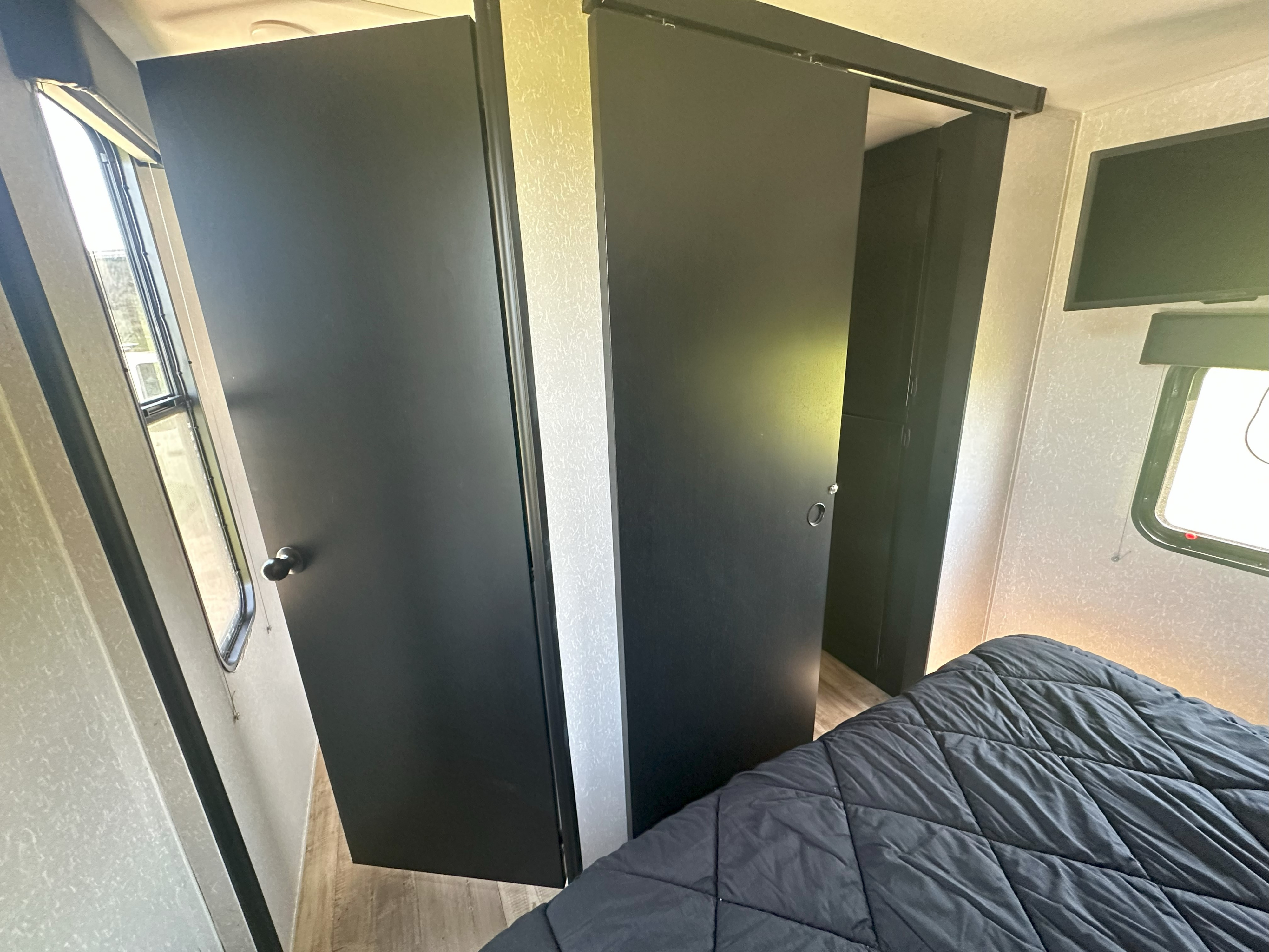 Modern RV rental interior showing black doors: a swing door and a sliding barn door, with a bed, TV, and window visible.. Forest River Cherokee 2022