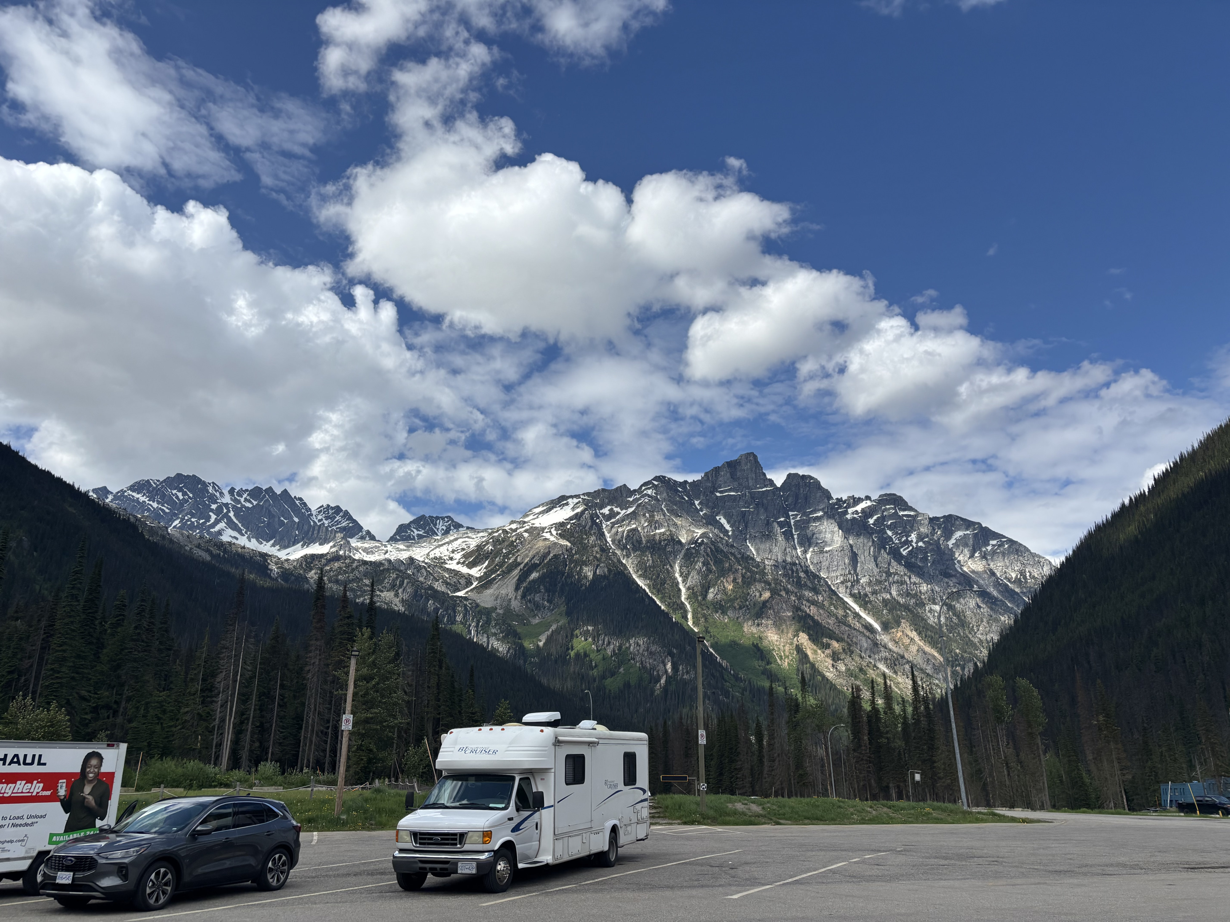 An RV rental and SUV parked in a mountain lot with snowy peaks & forests under a blue sky, perfect for a scenic road trip.. Gulf Stream BT Cruiser 2004