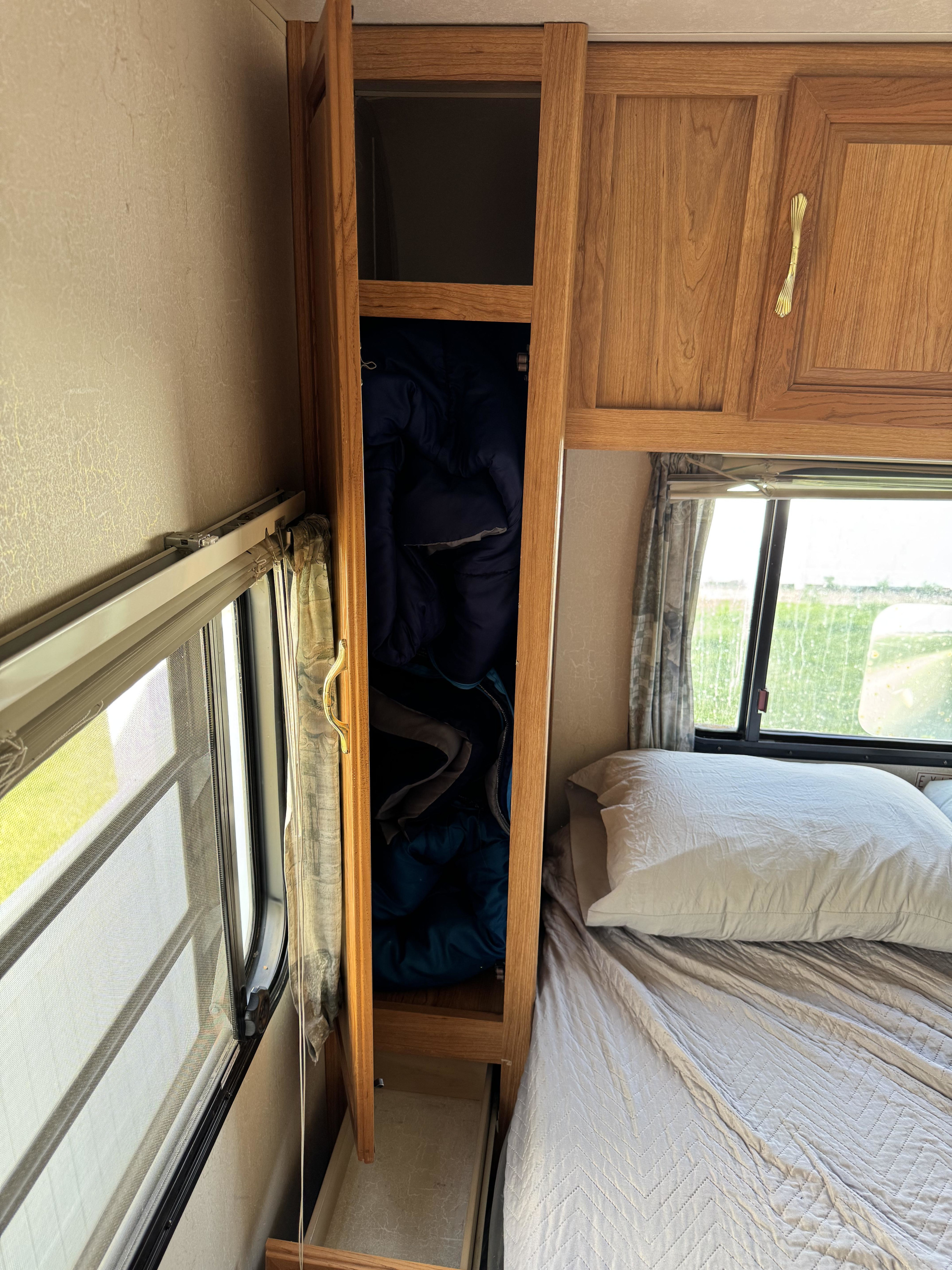 RV rental bedroom: bed, window view, and open storage cabinet with blue gear.. Coachmen Leprechaun 2001