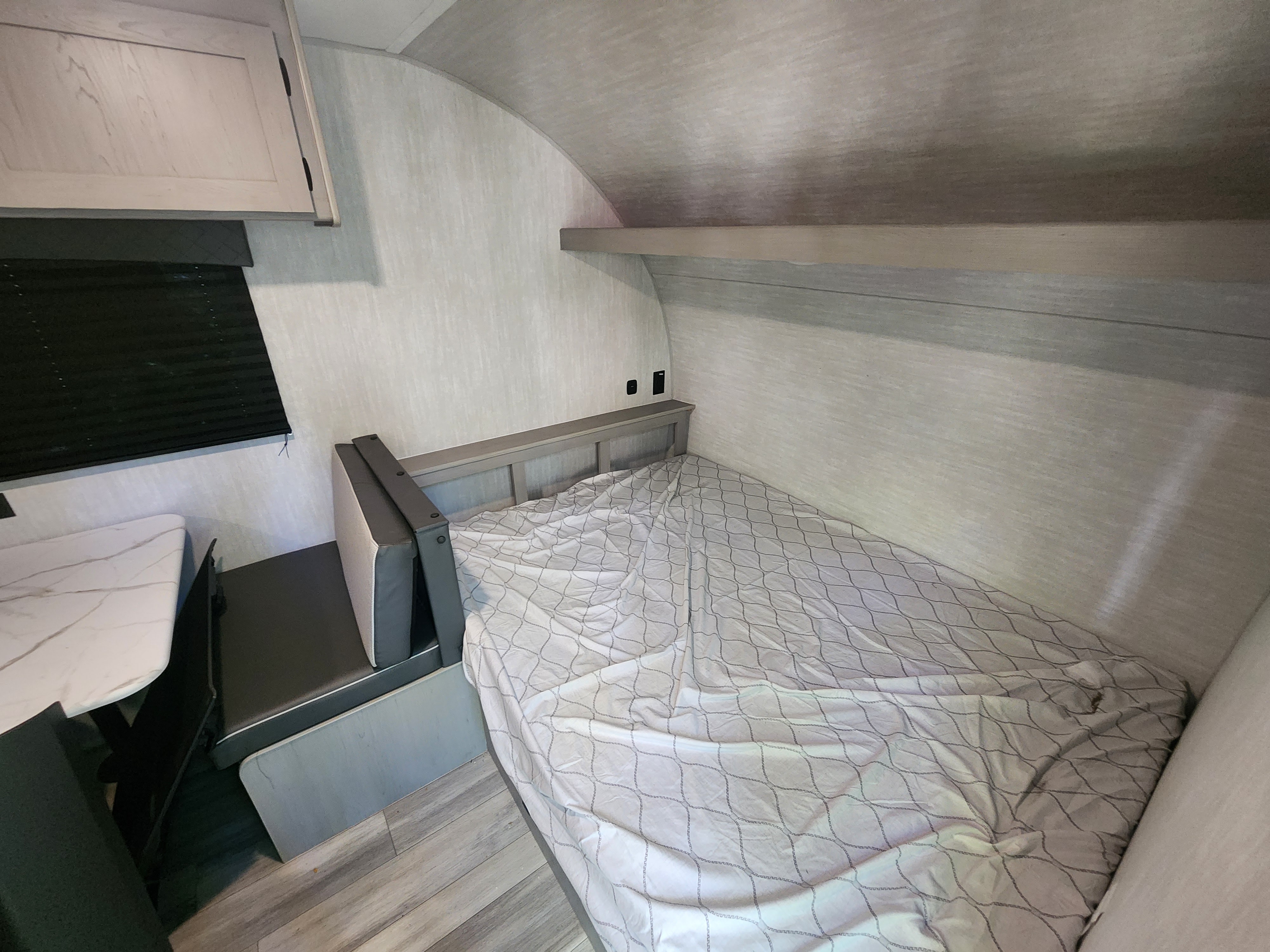 Bright RV rental interior: A bed with a patterned comforter, small dinette, and overhead cabinet are visible.. Coachmen RV Clipper 3k 2025