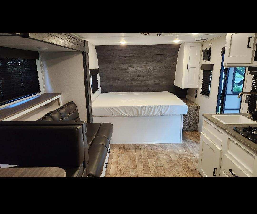 This modern RV rental interior offers a comfy bed, functional kitchen with sink & stovetop, and a cozy dinette area.. Keystone RV Hideout 2021