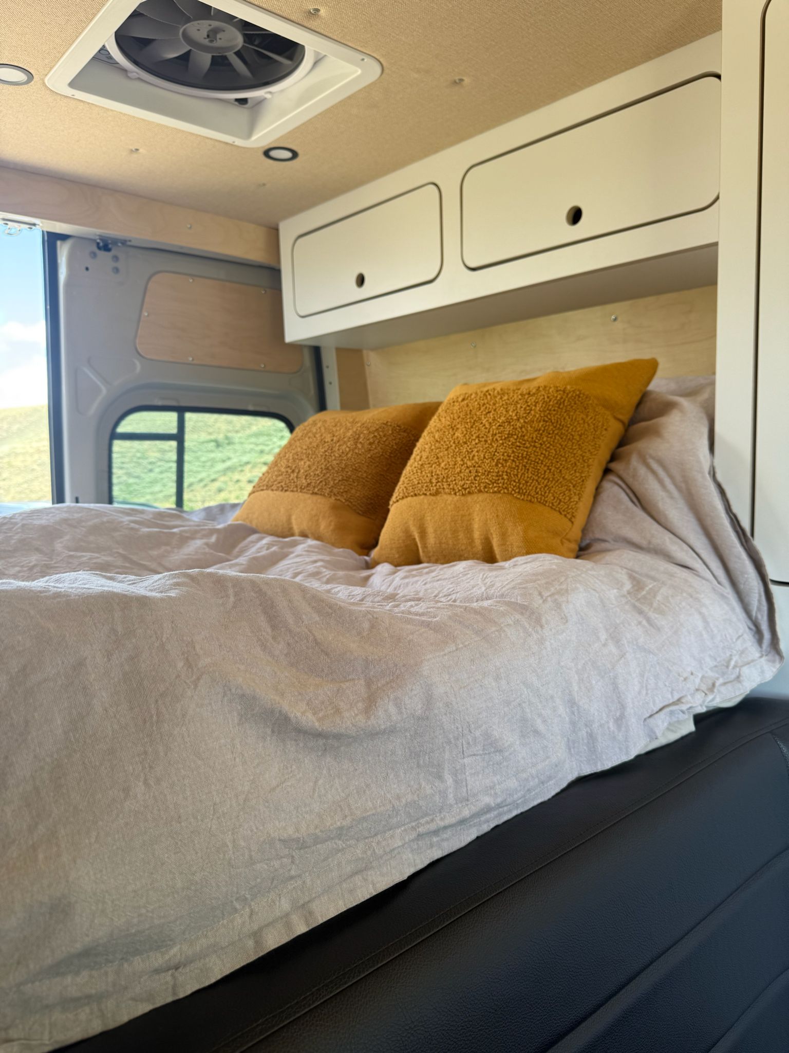 Cozy RV rental sleeping area with mustard pillows, ample storage, and a picturesque window view.. Mercedes-Benz Allterra AWD 2025