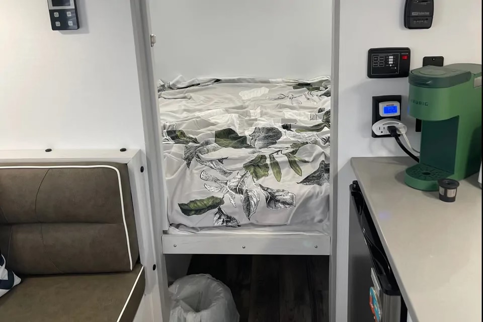 Cozy RV rental interior with a compact kitchenette, green Keurig, comfy bunk bed featuring leafy bedding, and cushioned seating.. Travel Lite Rove Litre 2024