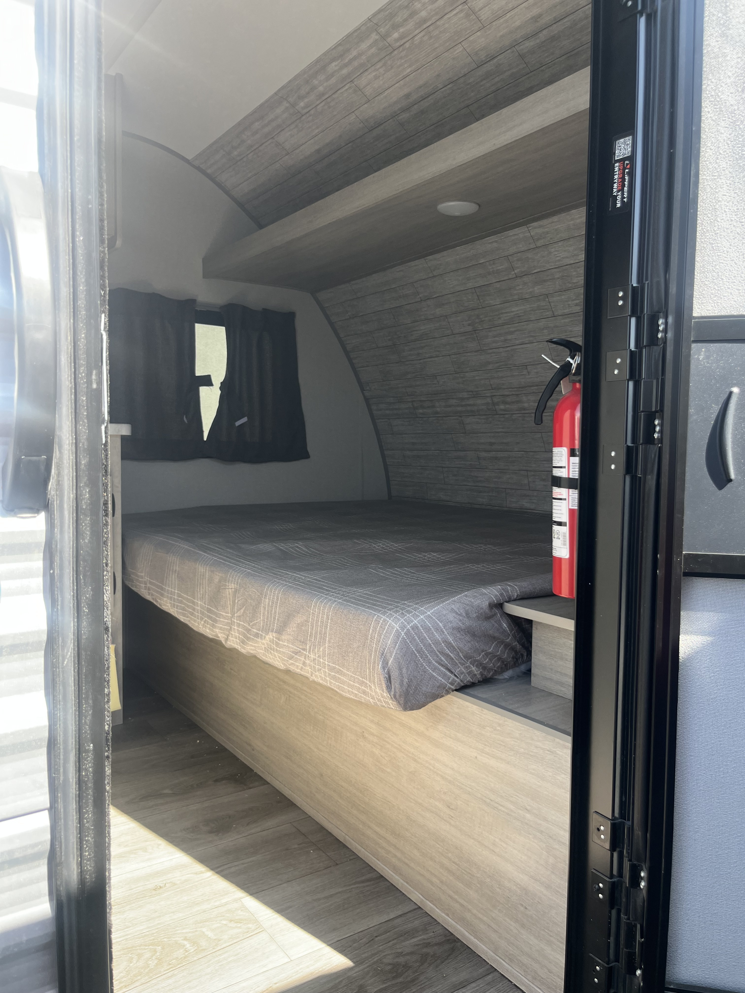 Cozy RV rental interior: bed, fire extinguisher, and wood-paneled walls inside a compact travel trailer.. Forest River Coachman Catalina 2025