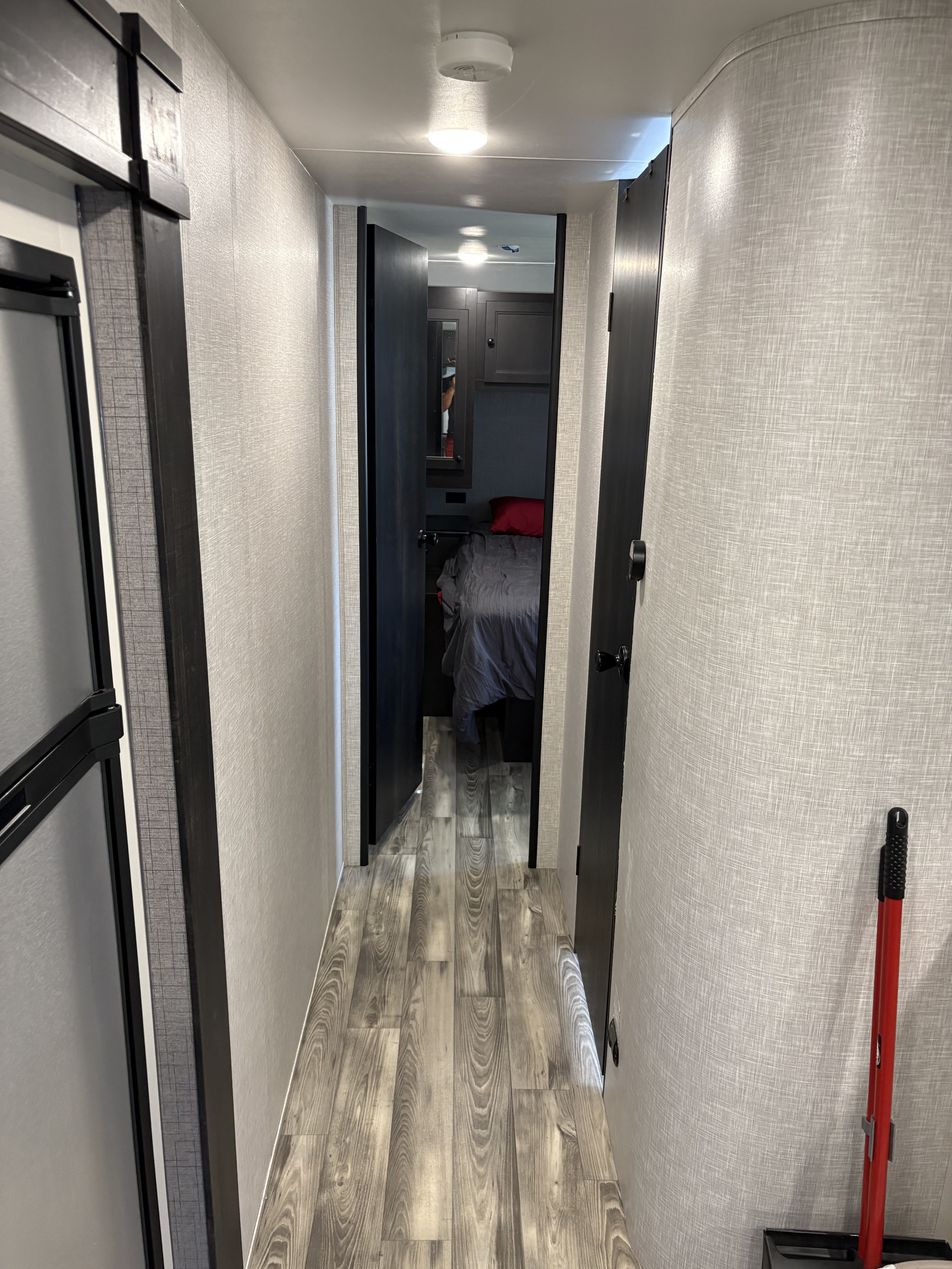 Inside an rv rental: A narrow hallway with light walls, wood-look floor, leading to a bedroom. Shows compact design & fridge.. Highland Ridge RV Open Range 2023