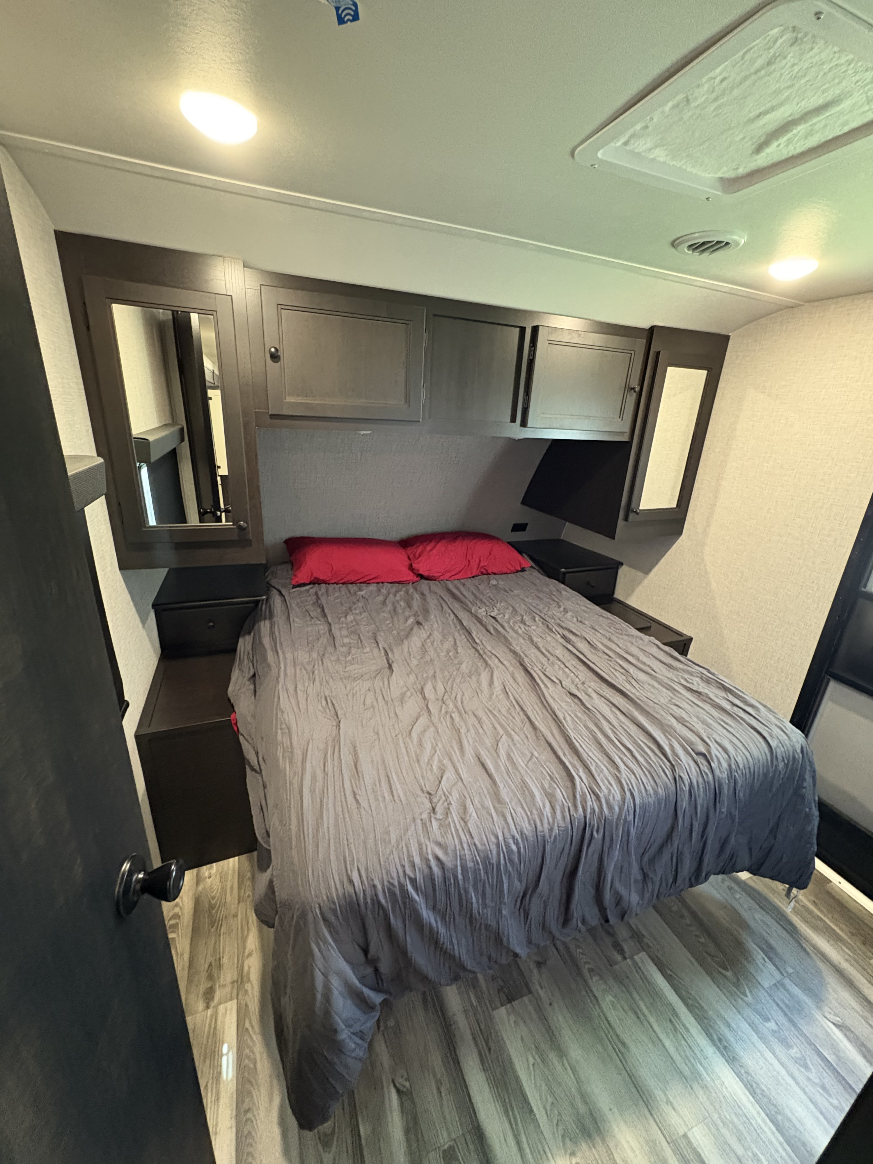This RV rental bedroom features a neatly made bed with red pillows, dark wooden cabinets, and modern lighting.. Highland Ridge RV Open Range 2023