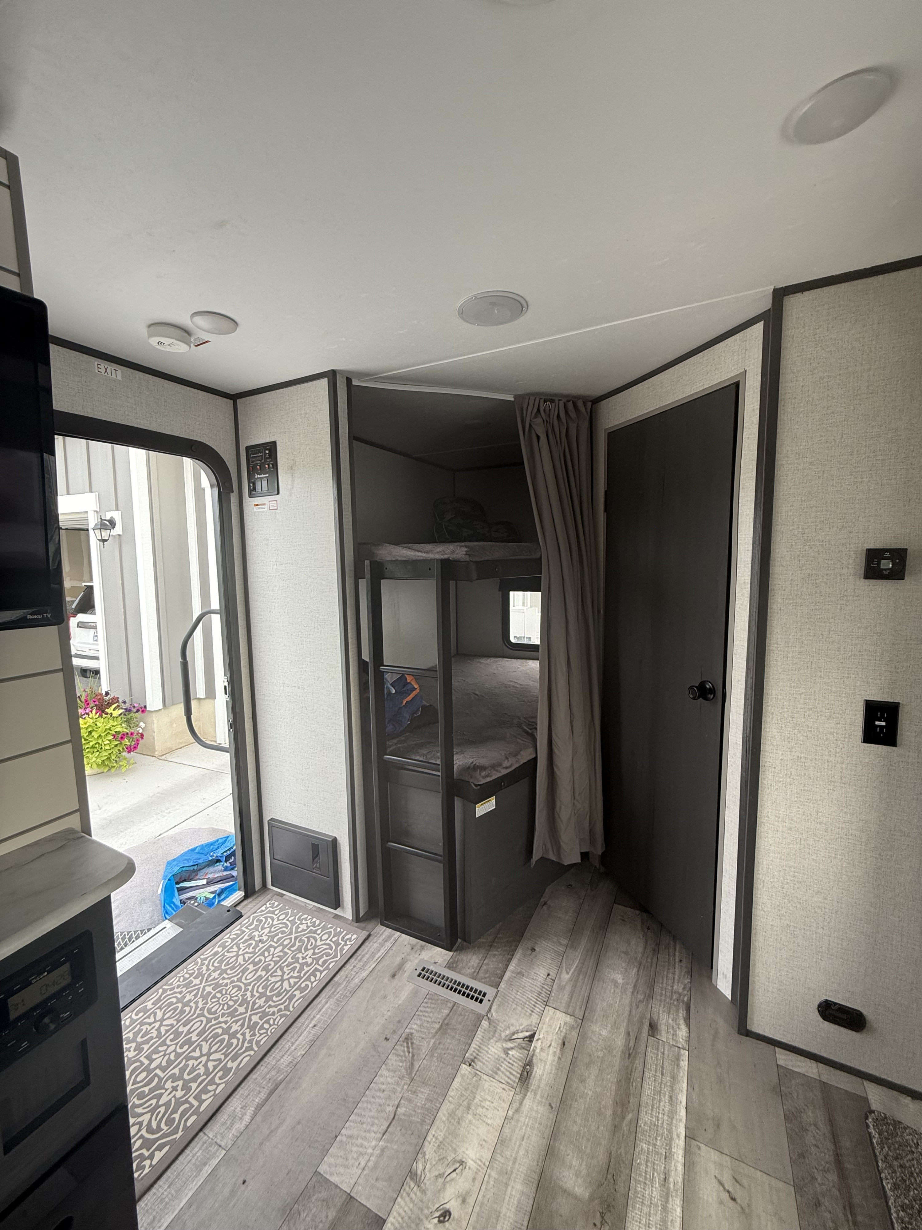 Modern RV rental interior with bunk beds, gray walls, and wood-look floor near an open entryway.. Aspen Trail Aspen Trail Trailer 2021