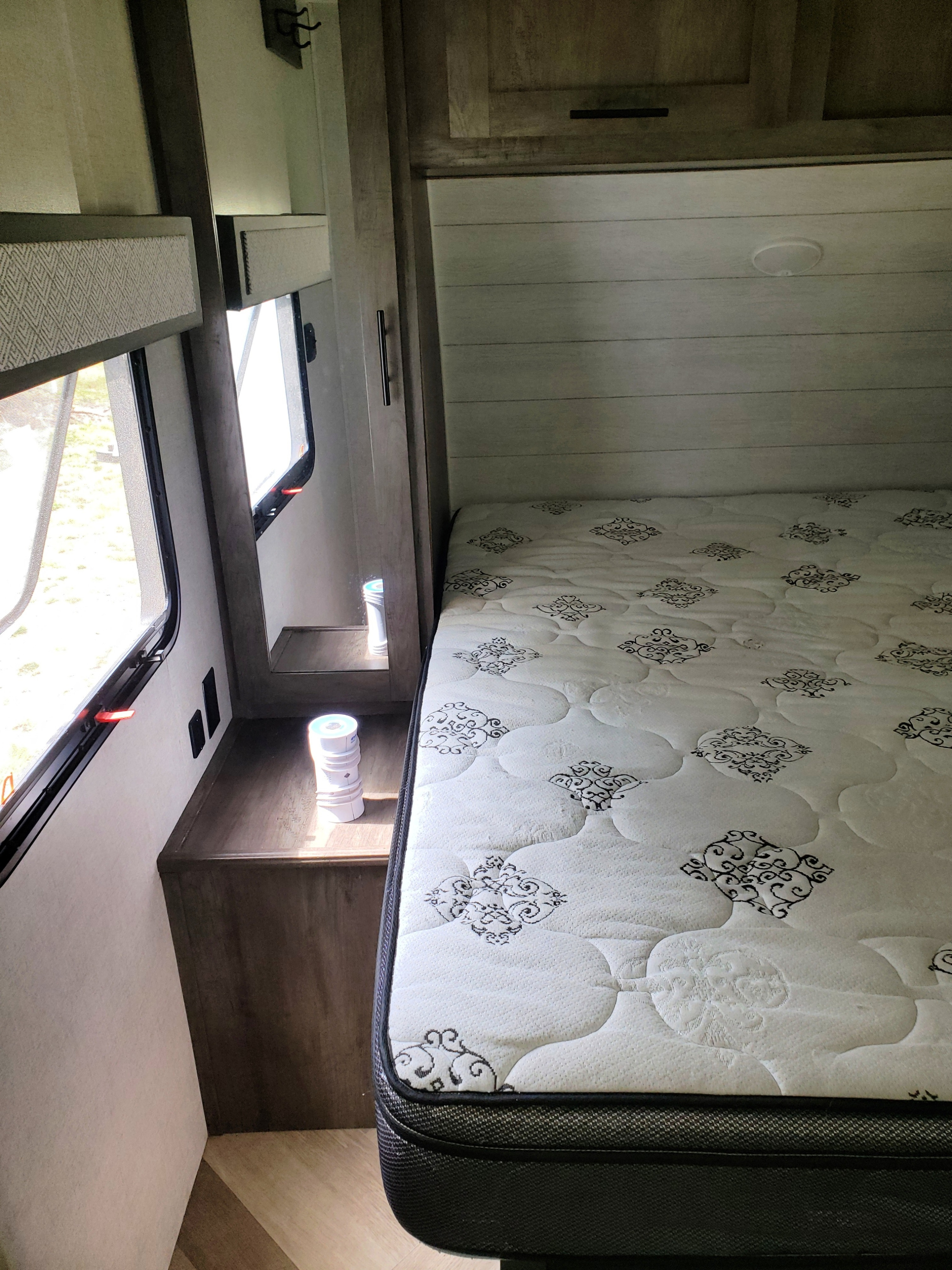 Step inside this cozy RV rental bedroom. It features a patterned mattress, window, and handy nightstand with outlets.. Forest River Wildwood 2020