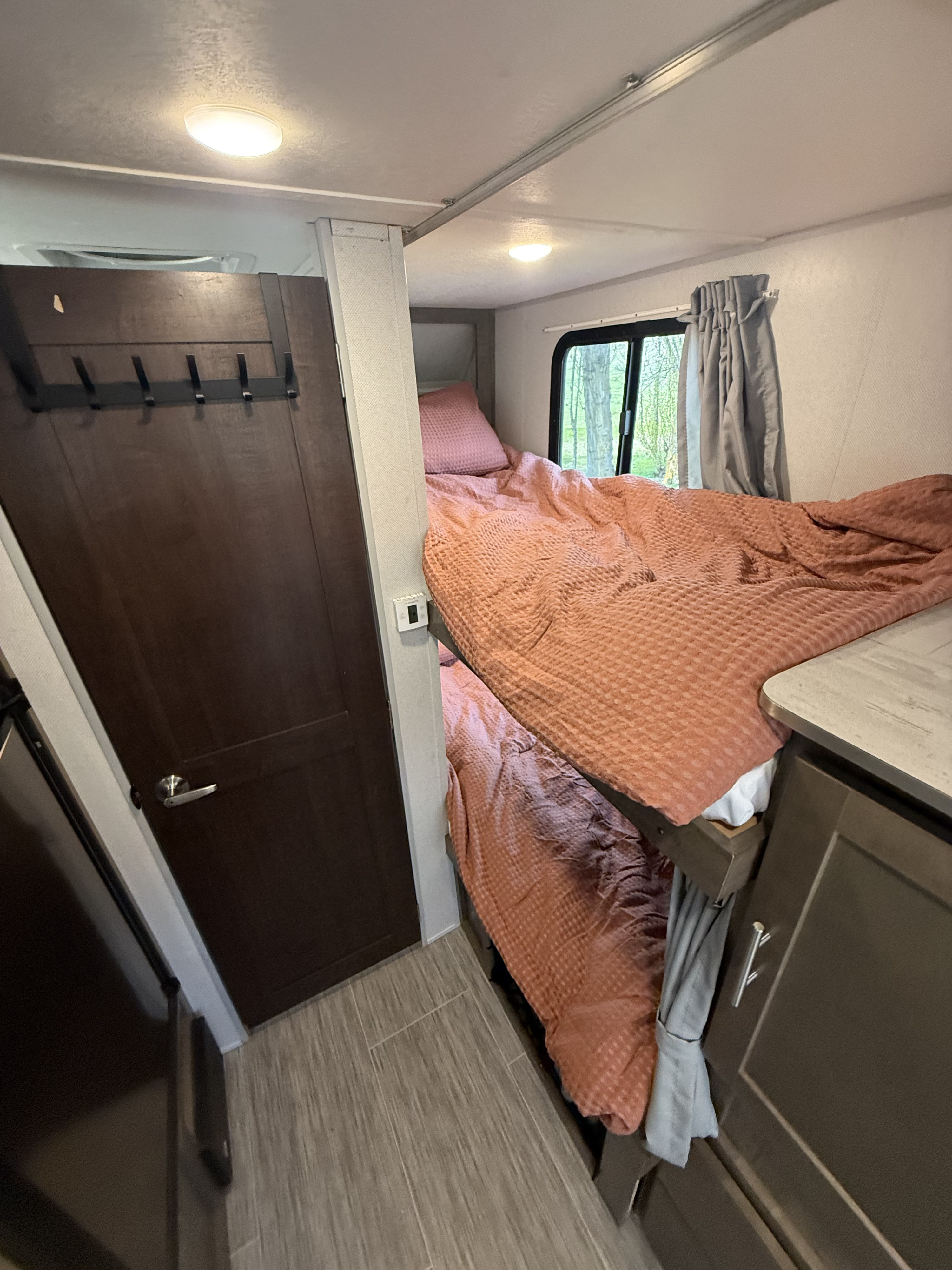 Inside an RV rental: comfortable bunk beds with peach quilts, a door, and a glimpse of nature outside.. Forest River No Boundaries 2019