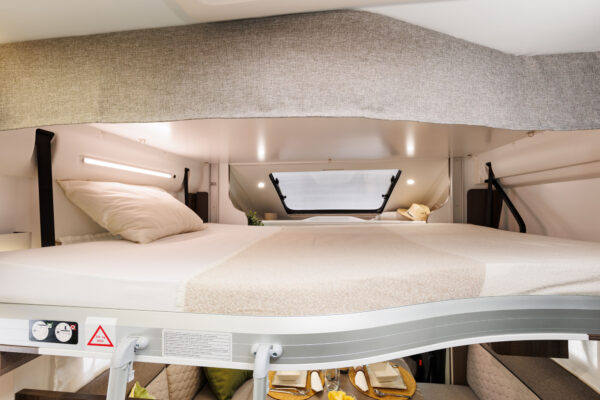 Interior of an RV rental showing a comfortable overhead bed with reading light, positioned above a dinette area.. BENIMAR T 497 TESSORO 2025