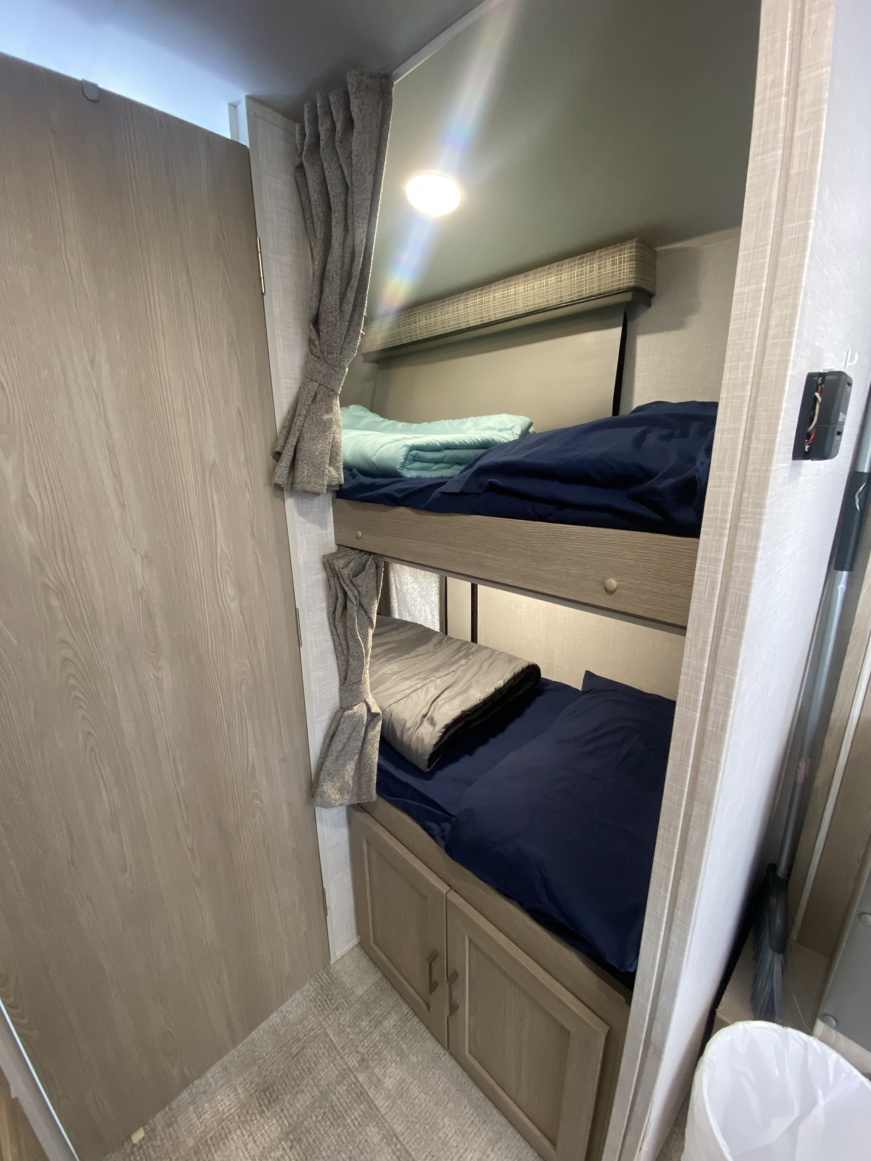 Compact rv rental bunk beds with blue and grey bedding, tied-back curtains, and lower storage cabinets.. Forest River Flagstaff E-Pro 2021