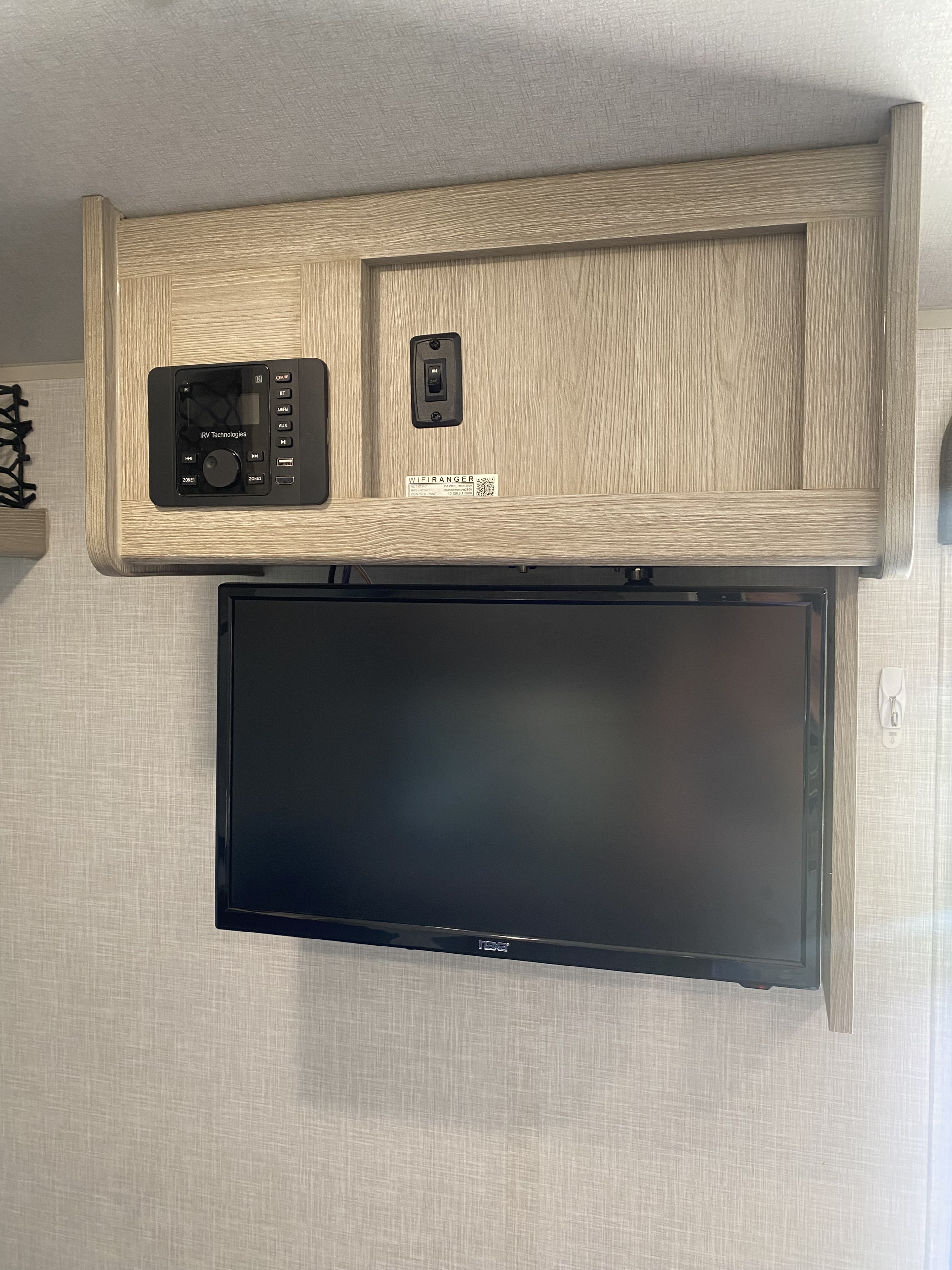 RV rental entertainment system featuring a mounted TV, iRV stereo, and WiFi details within a light wood cabinet.. Forest River Flagstaff E-Pro 2021