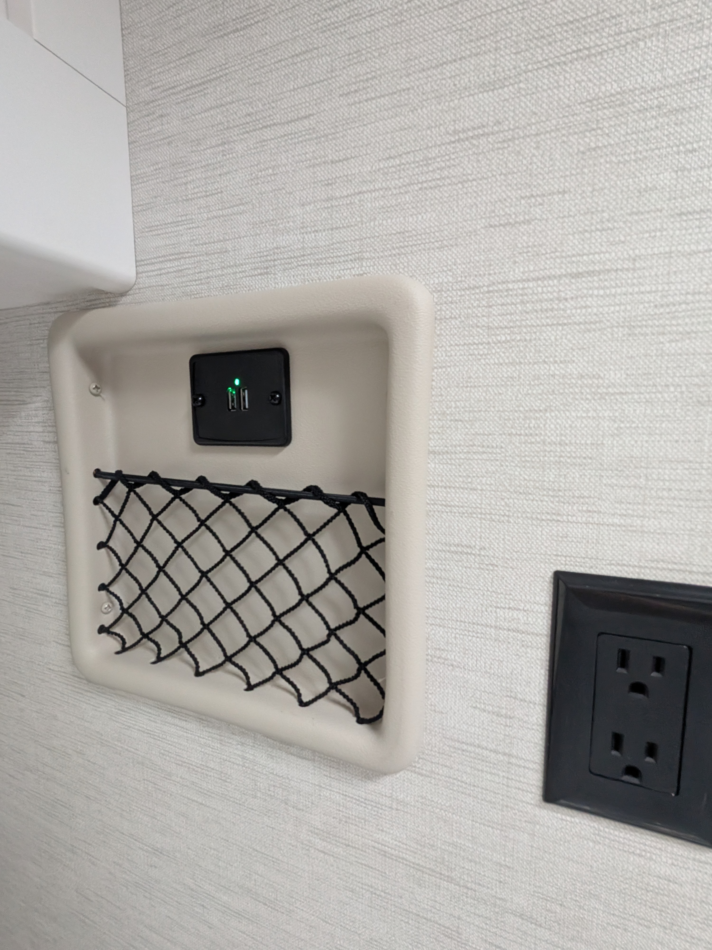 RV rental: Textured wall features a beige storage pocket with glowing USB ports, mesh net, and a black power outlet.. Thor Eddie Bauer 2025