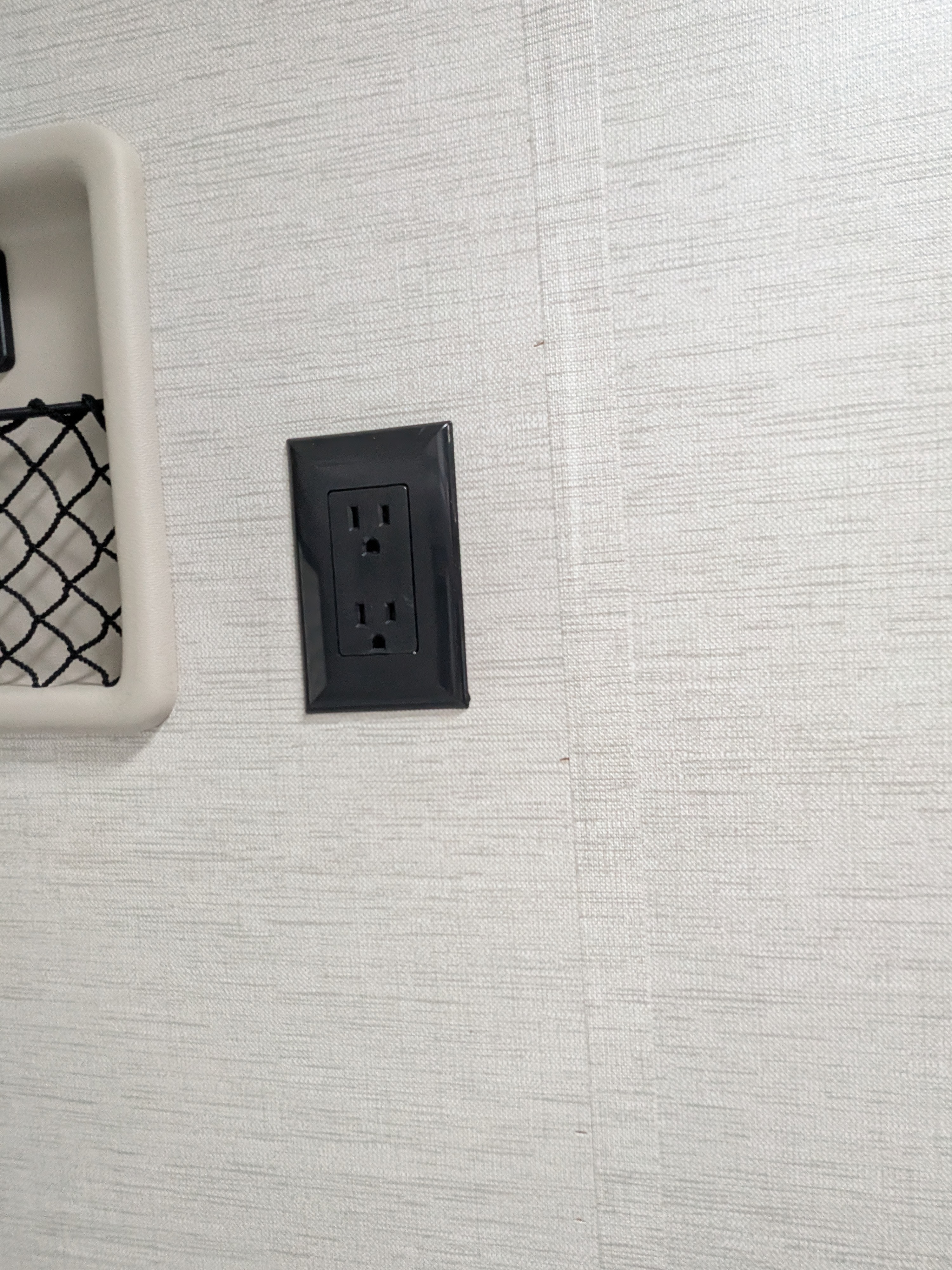 Modern RV rental interior showing a textured wall, black power outlet, and built-in storage net for convenient use.. Thor Eddie Bauer 2025