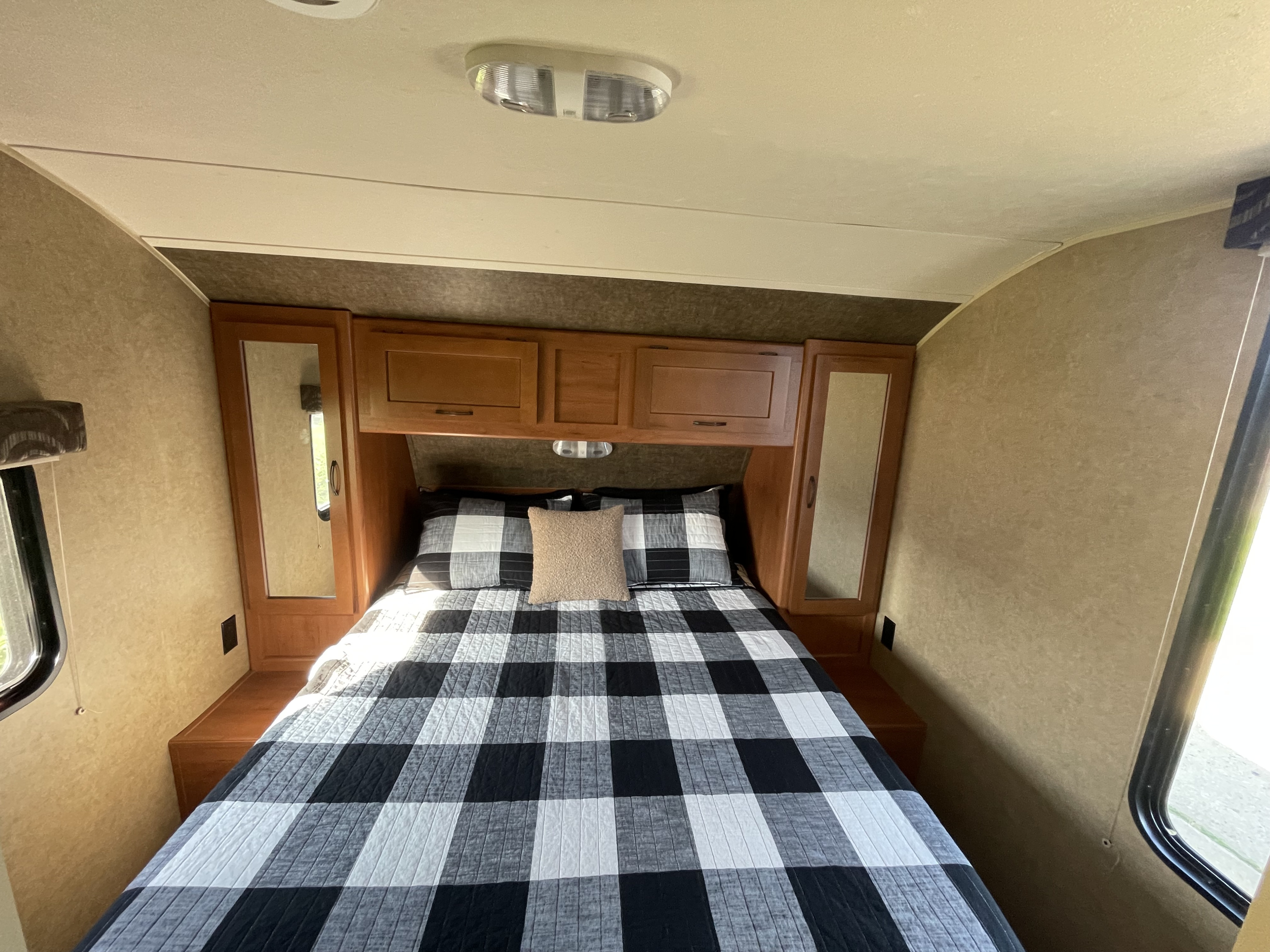 Cozy RV rental bedroom with a black and white checkered comforter, wooden cabinets, and bright window light.. Forest River Cherokee 2015