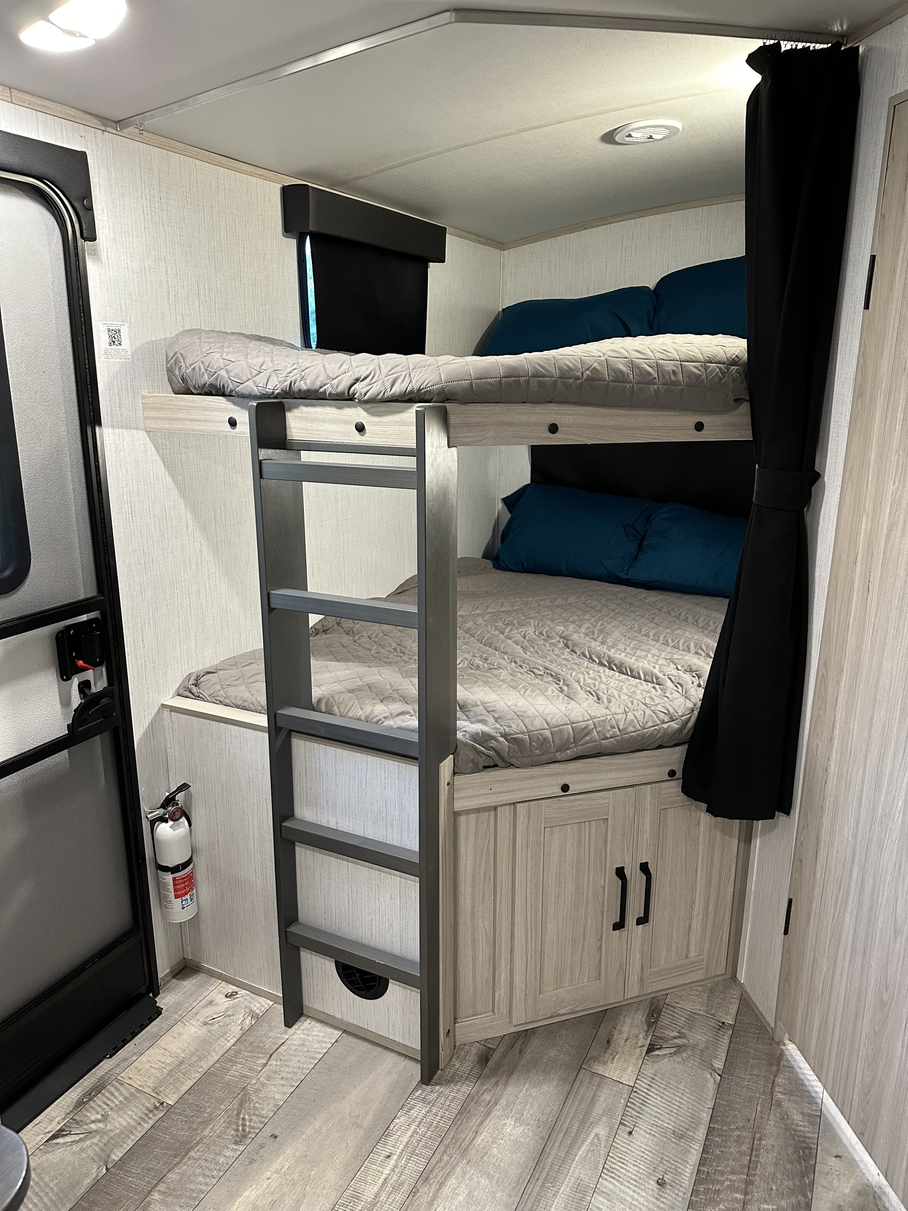 RV rental bunk beds with cozy bedding, a ladder, and a safety fire extinguisher are visible inside.. Heartland RVs Sundance Ultra Lite 2022