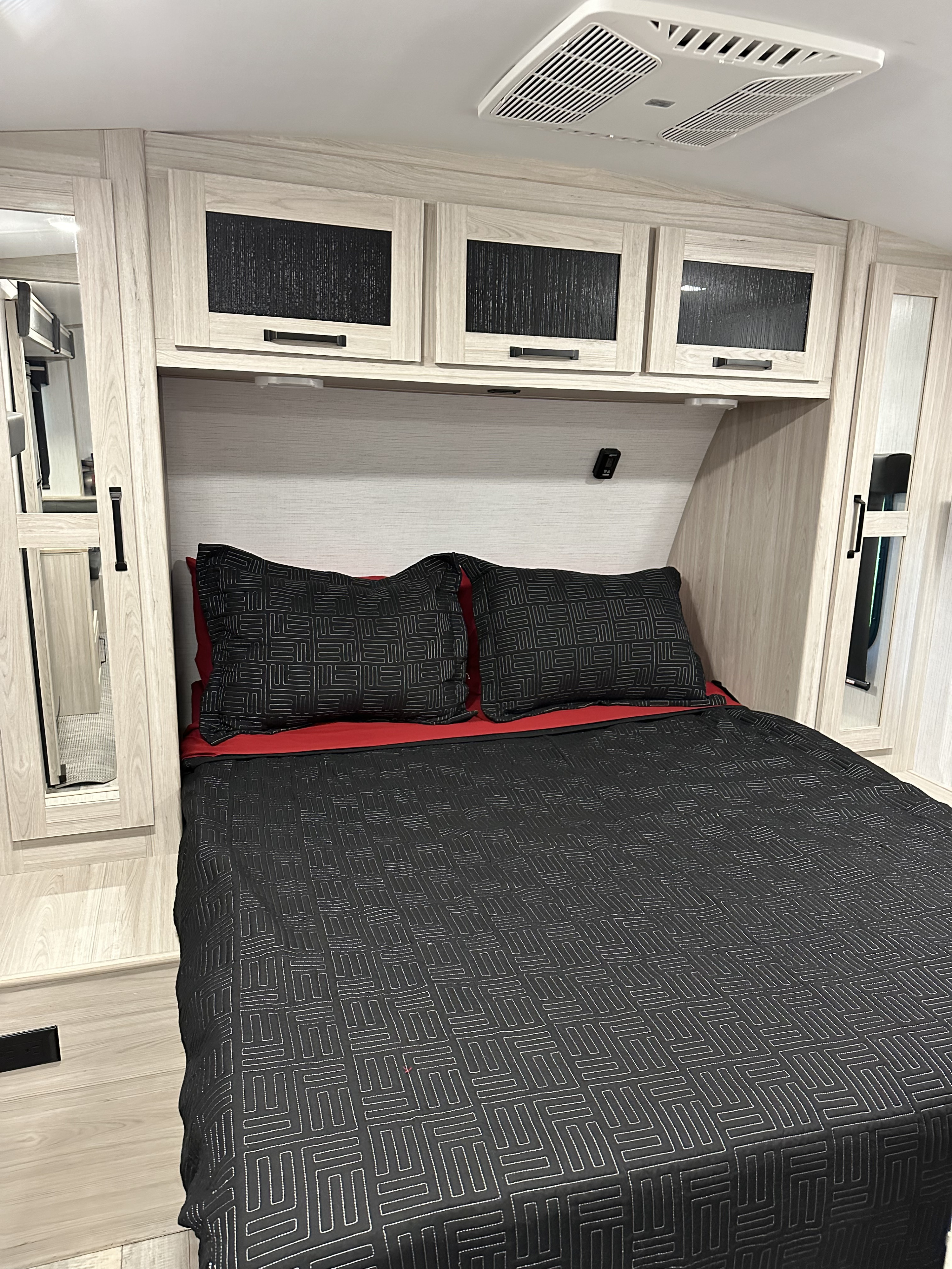 This RV rental features a compact bedroom with a modern bed, overhead cabinets, and AC unit, ideal for travel.. Heartland RVs Sundance Ultra Lite 2022