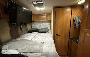 RV rental bedroom featuring a large bed with grey bedding, overhead TV, and wooden cabinets. Ideal for travel.. Thor Majestic 2013