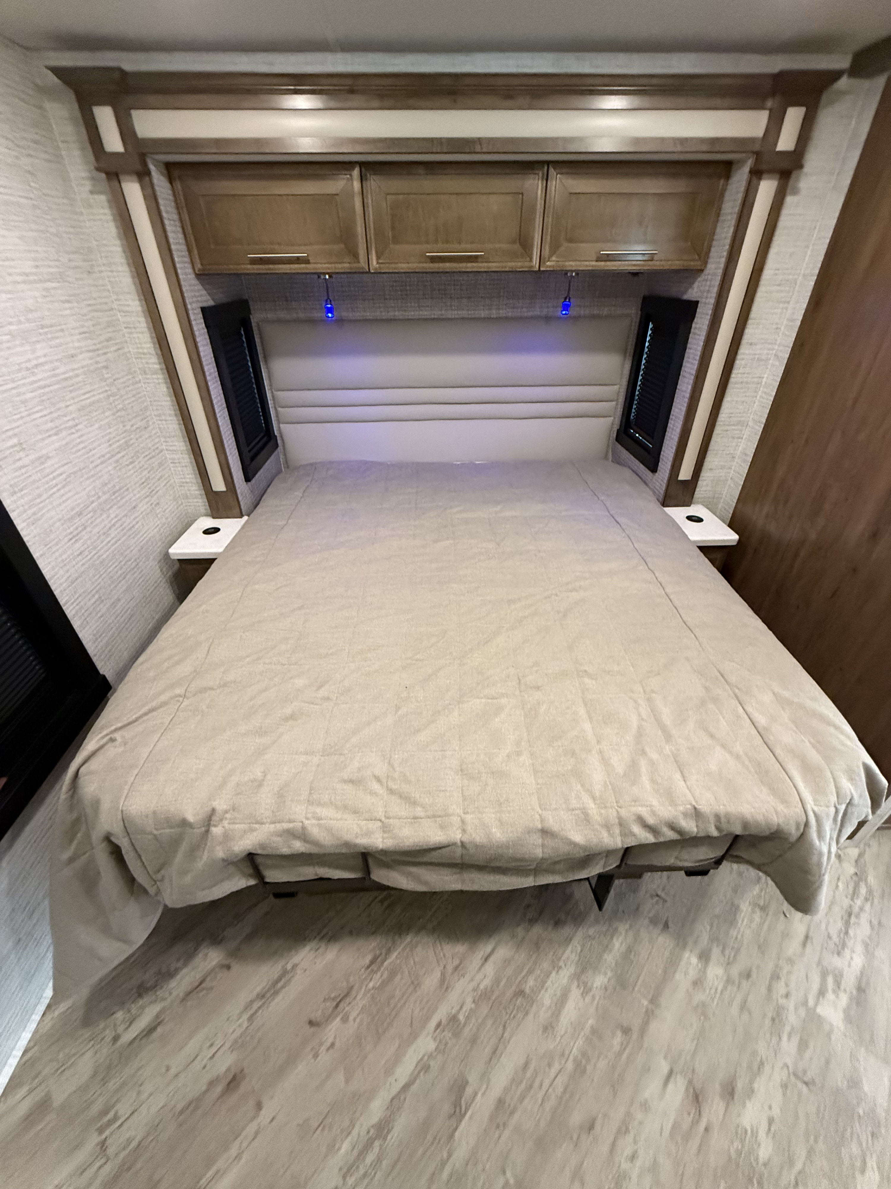 RV rental bedroom: light bed, upholstered headboard, wood overhead cabinets, and blue accent lights illuminate.. Jayco Seneca 2025