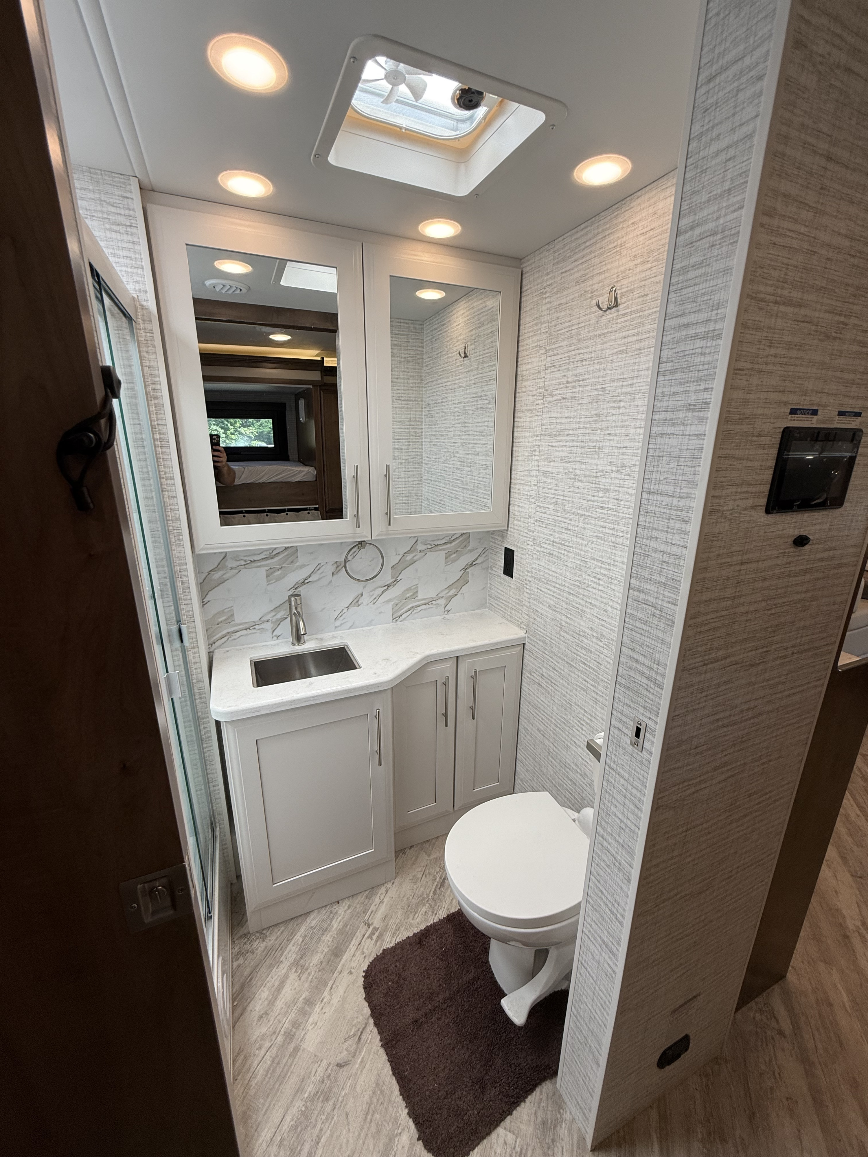 Inside an RV rental: a compact bathroom with a modern vanity, sink, toilet, and glass shower, illuminated by bright lights.. Jayco Seneca 2025