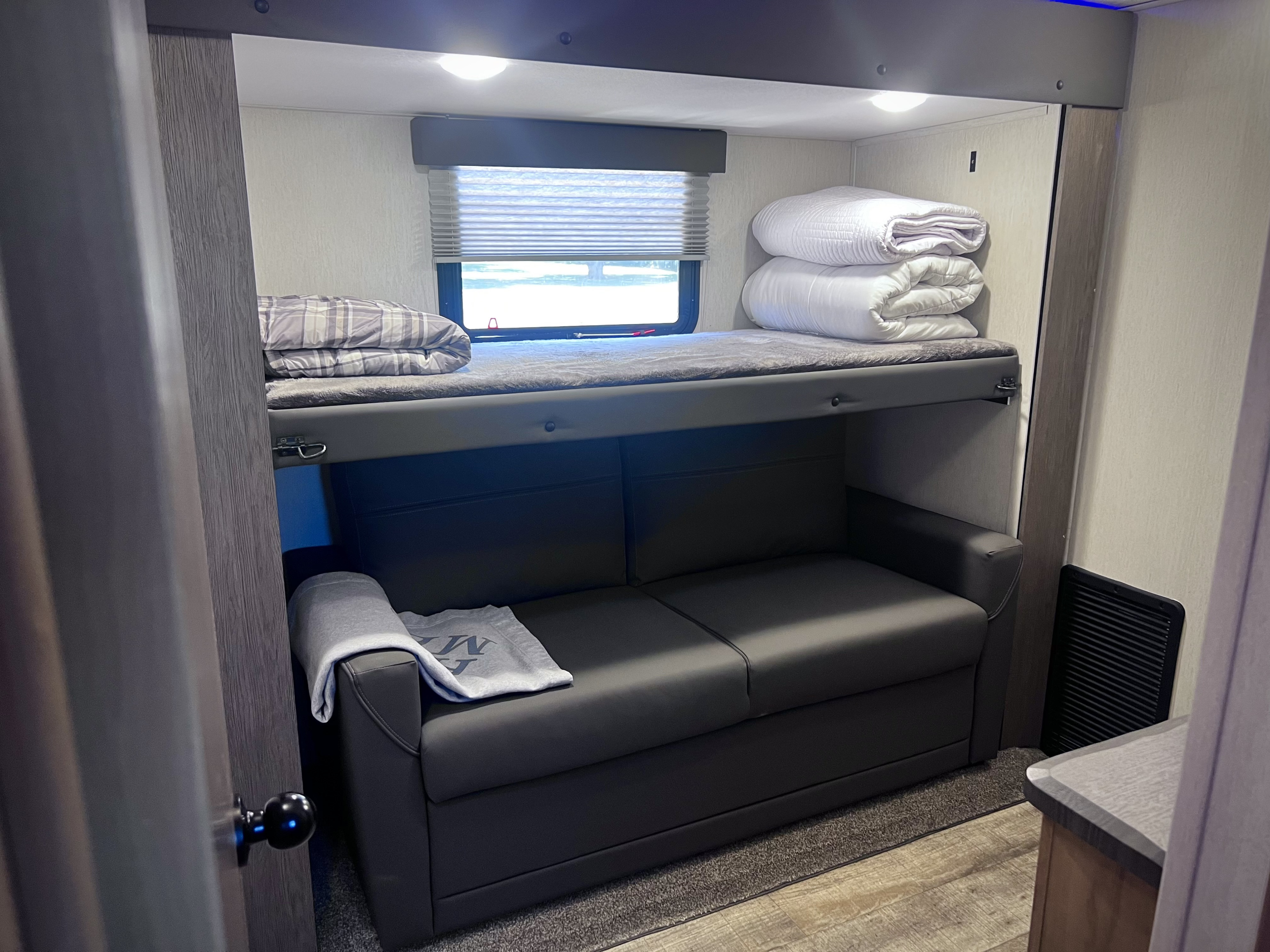 Inside an RV rental: a cozy bunk bed with fresh linens above a dark convertible sofa, perfect for compact living.. Forest River Cherokee Arctic Wolf 3660 Suite 2024