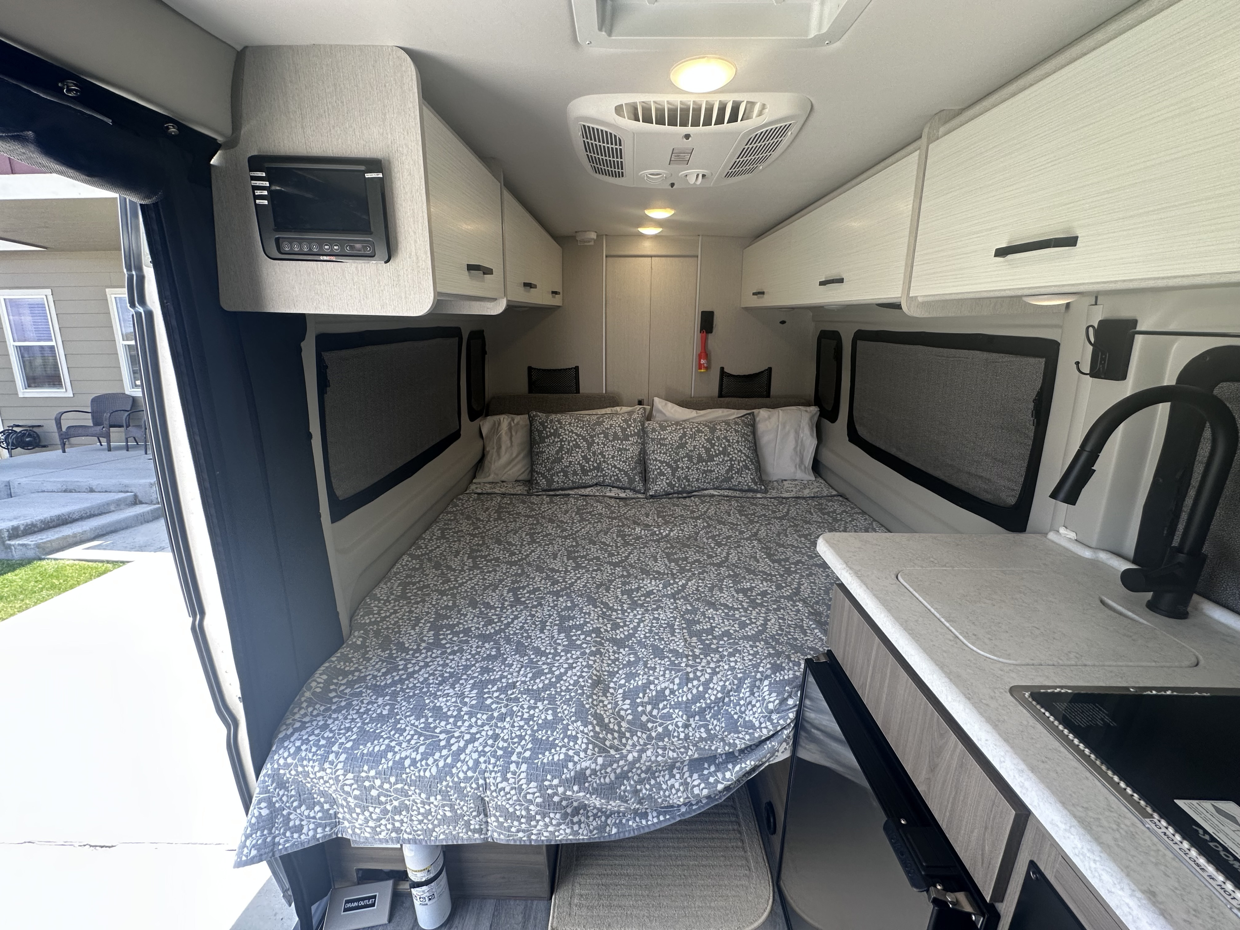 This RV rental interior showcases a comfy bed, compact kitchen with sink/stove, and overhead cabinets.. Thor Dazzle 2024