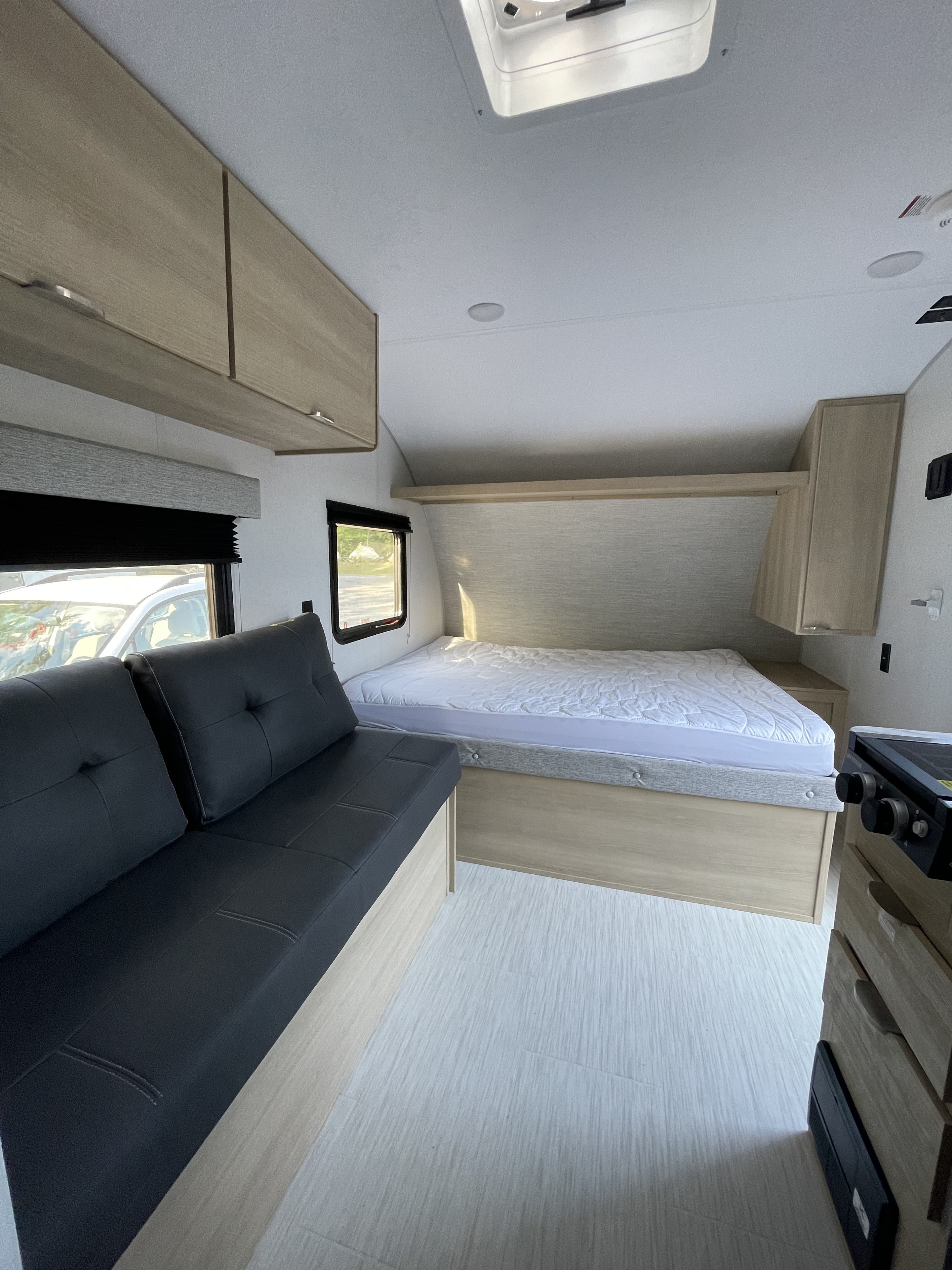 Modern RV rental interior featuring a cozy bed, black sofa, light wood cabinetry, and compact kitchenette.. Forest River Salem 2024