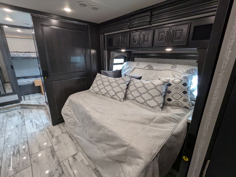 Inside an RV rental: A spacious bedroom with a queen-sized bed, decorative pillows, overhead storage, and a sliding door to bunk beds.. Fleetwood Discovery 2025
