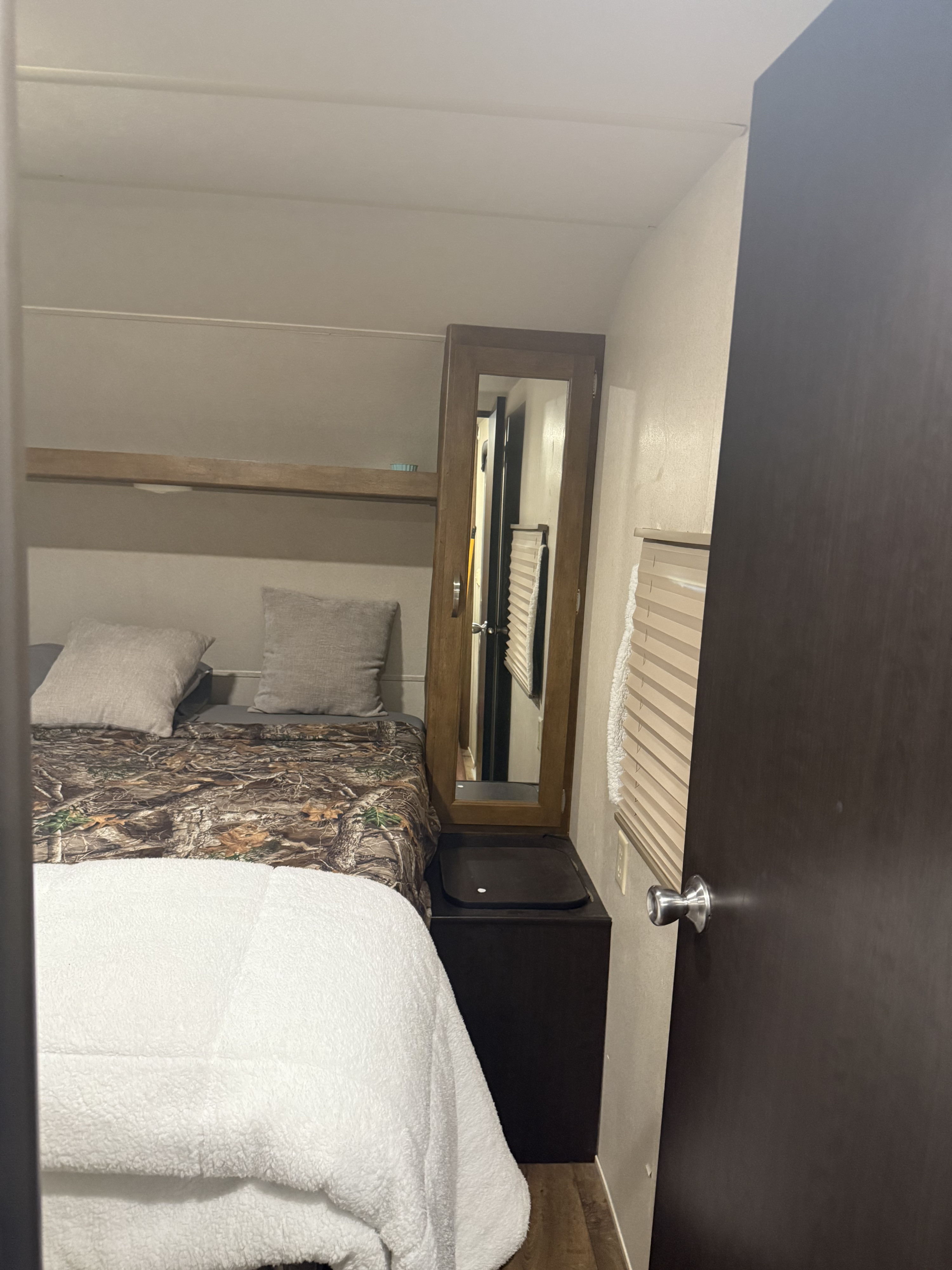 Cozy RV rental bedroom. Features a camo bed, mirror cabinet, storage, and window with blinds. Space-saving design.. Forest River Salem 2017