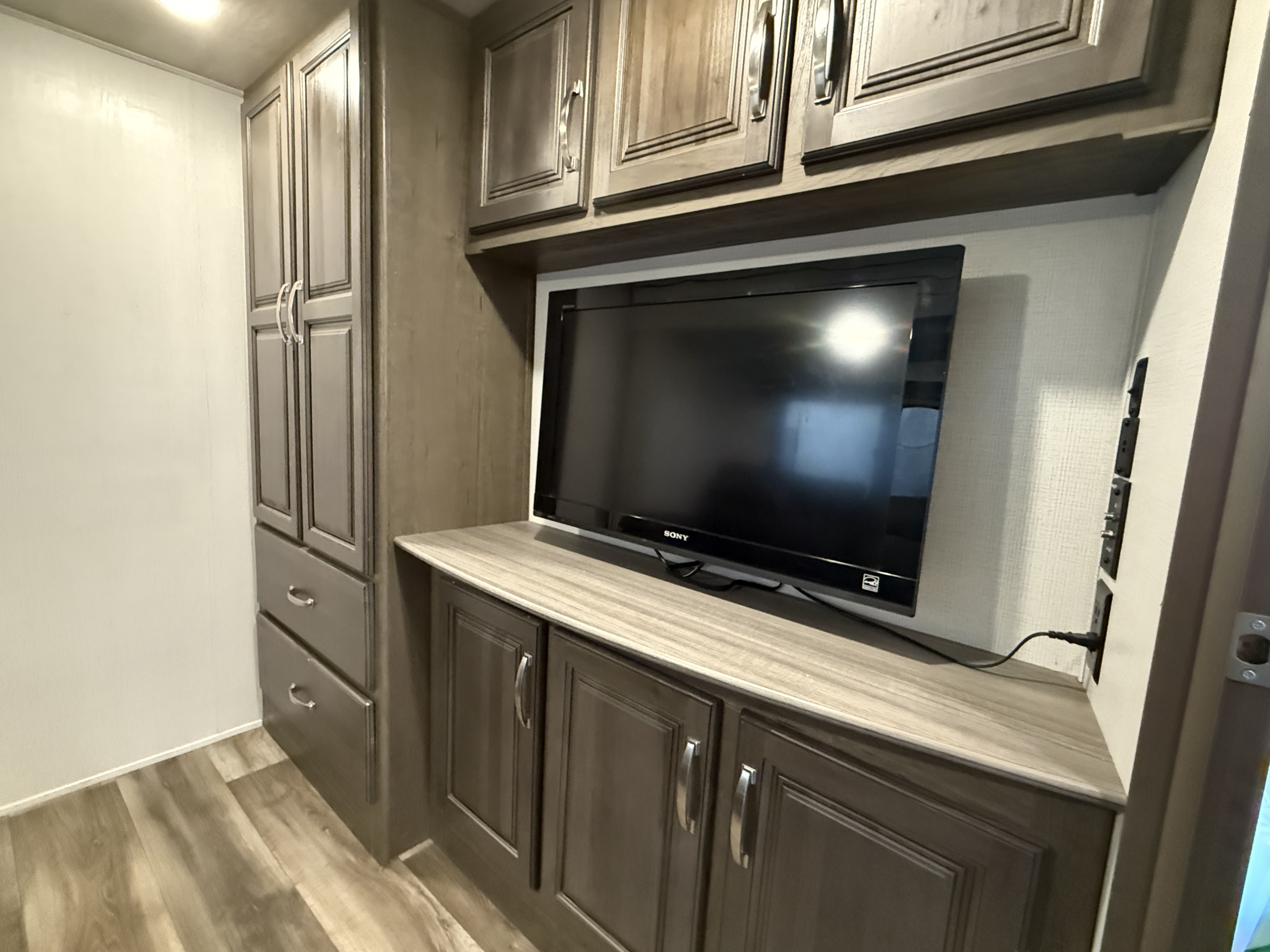 Inside an RV rental: view of the entertainment center with a TV, ample storage cabinets, and wood-look flooring.. Keystone RV Cougar 2022