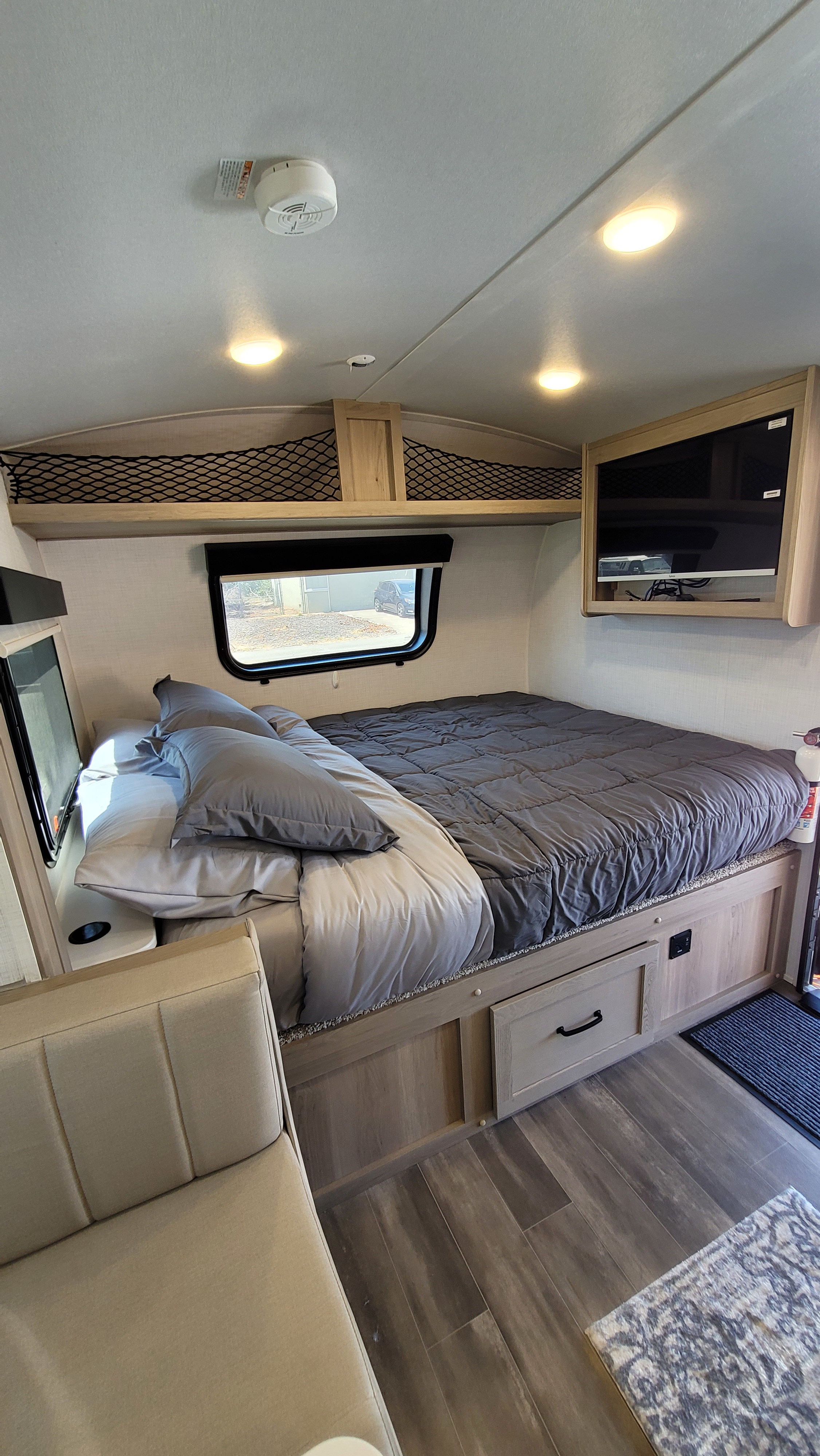 Cozy RV rental interior, showing a comfortable bed with grey bedding, wall-mounted TV, and practical storage solutions.. Forest River Rockwood Geo Pro 2024