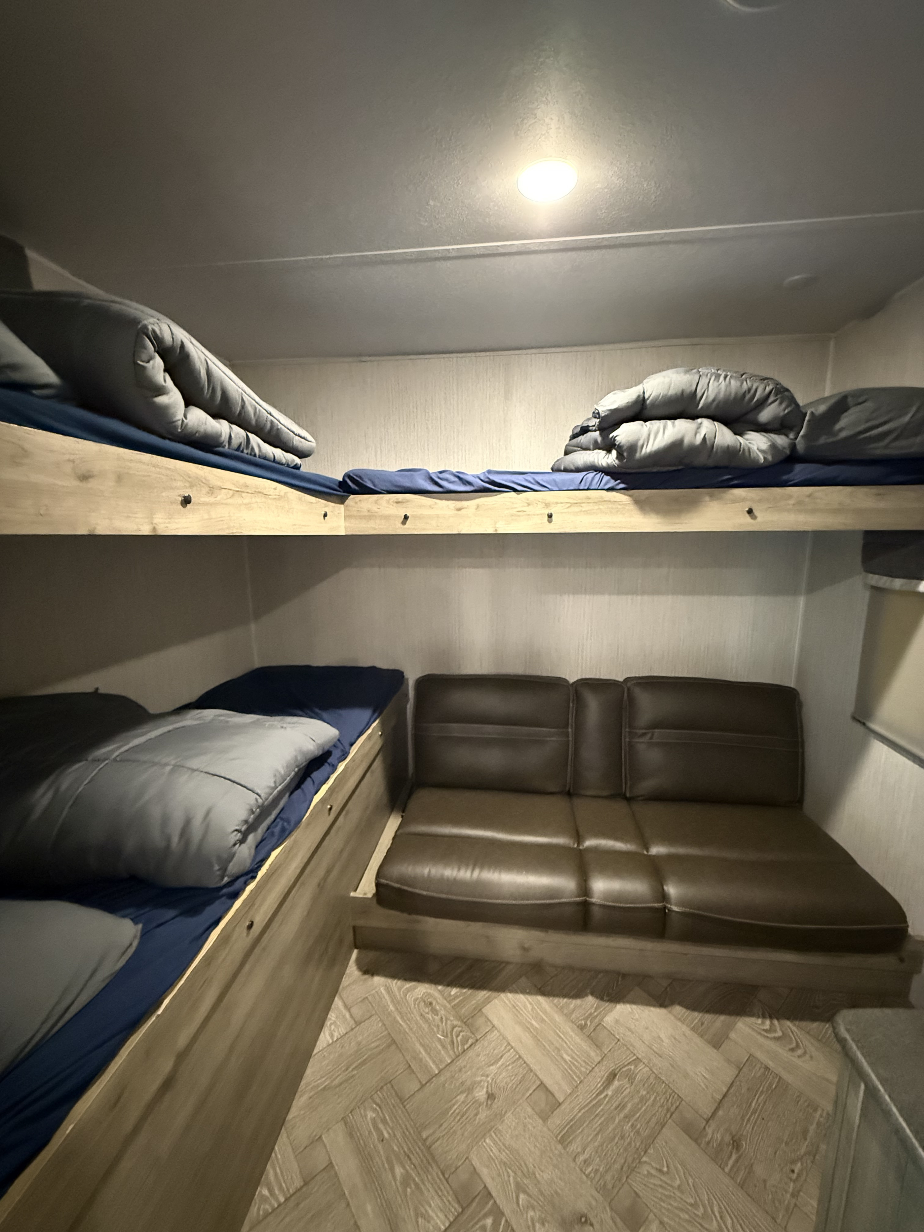 RV rental bunk beds & brown sofa in a compact interior, offering sleeping and lounge space.. Forest River Palomino Puma 2022