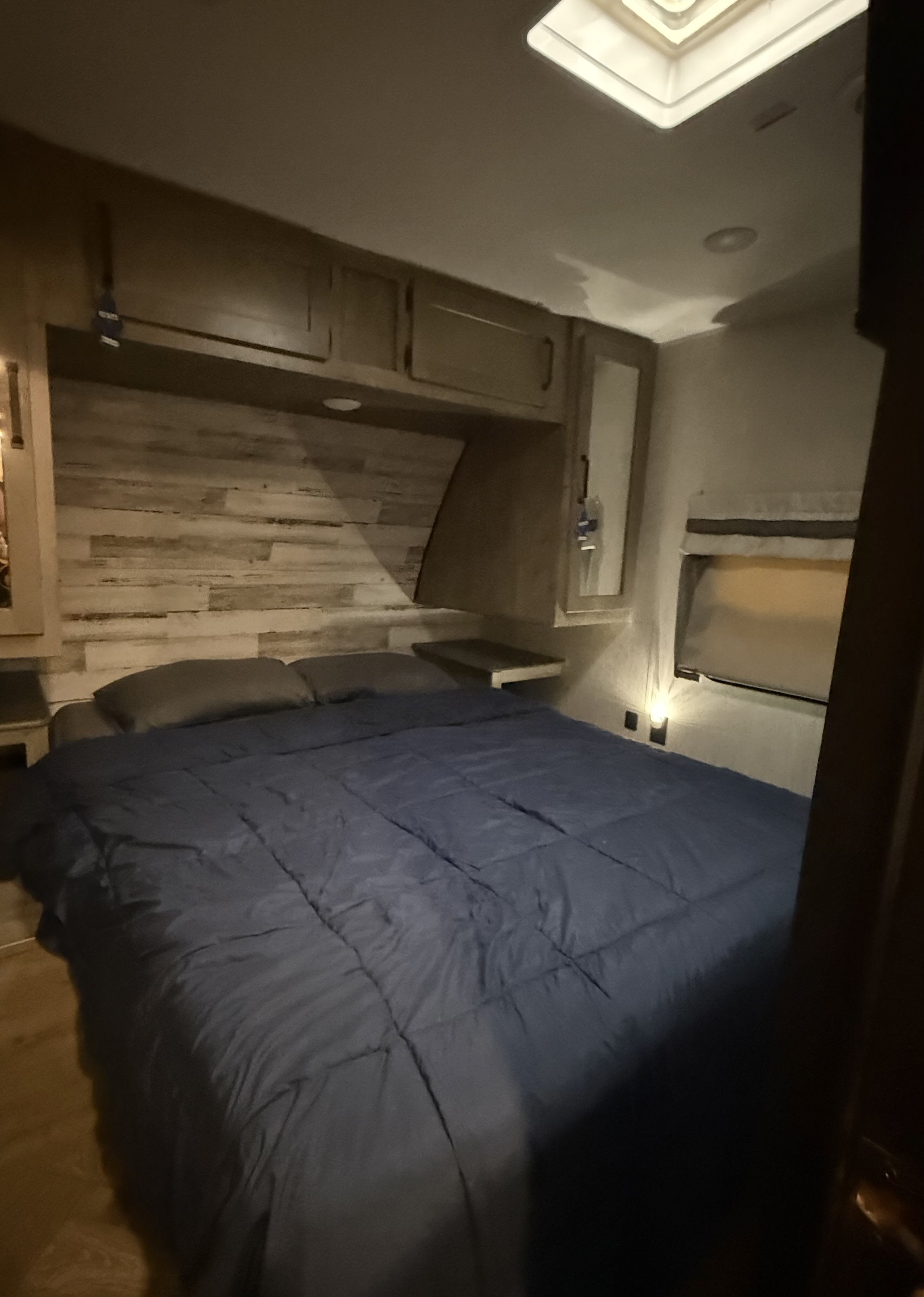 Cozy RV rental bedroom featuring a large bed, wood-paneled wall, overhead storage, window, and ceiling skylight.. Forest River Palomino Puma 2022