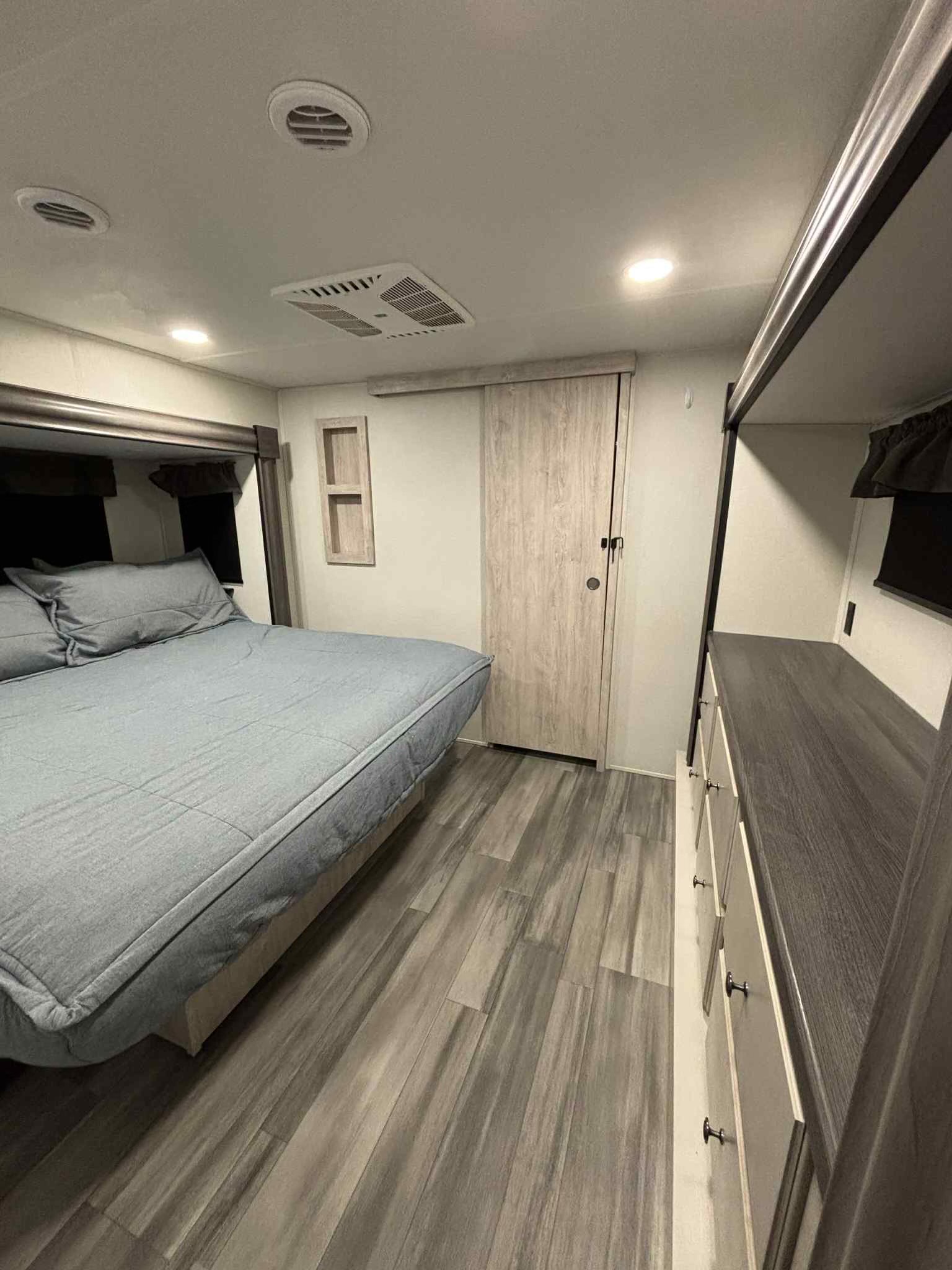 Spacious, modern RV rental bedroom with comfy gray bed, dresser, and light wood flooring. Perfect for your next trip.. Forest River Sandpiper 2024