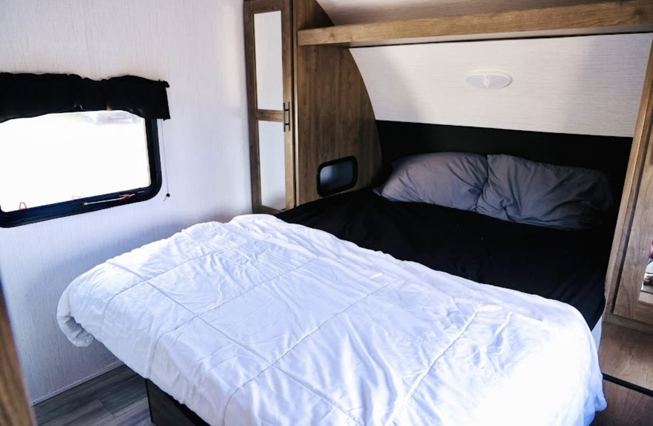 Step into this cozy RV rental bedroom, featuring a comfortable bed, window, and built-in storage.. Heartland RVs Pioneer 2024