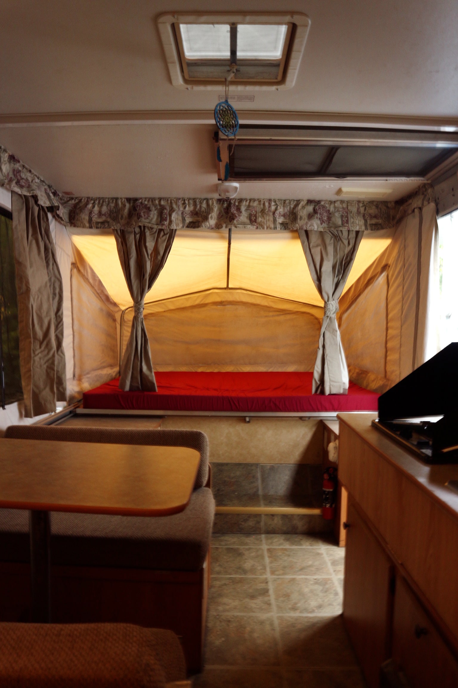 Cozy RV rental interior featuring a bright red bed, dining table with bench seating, and compact kitchen area.. Starcraft 1701 2006