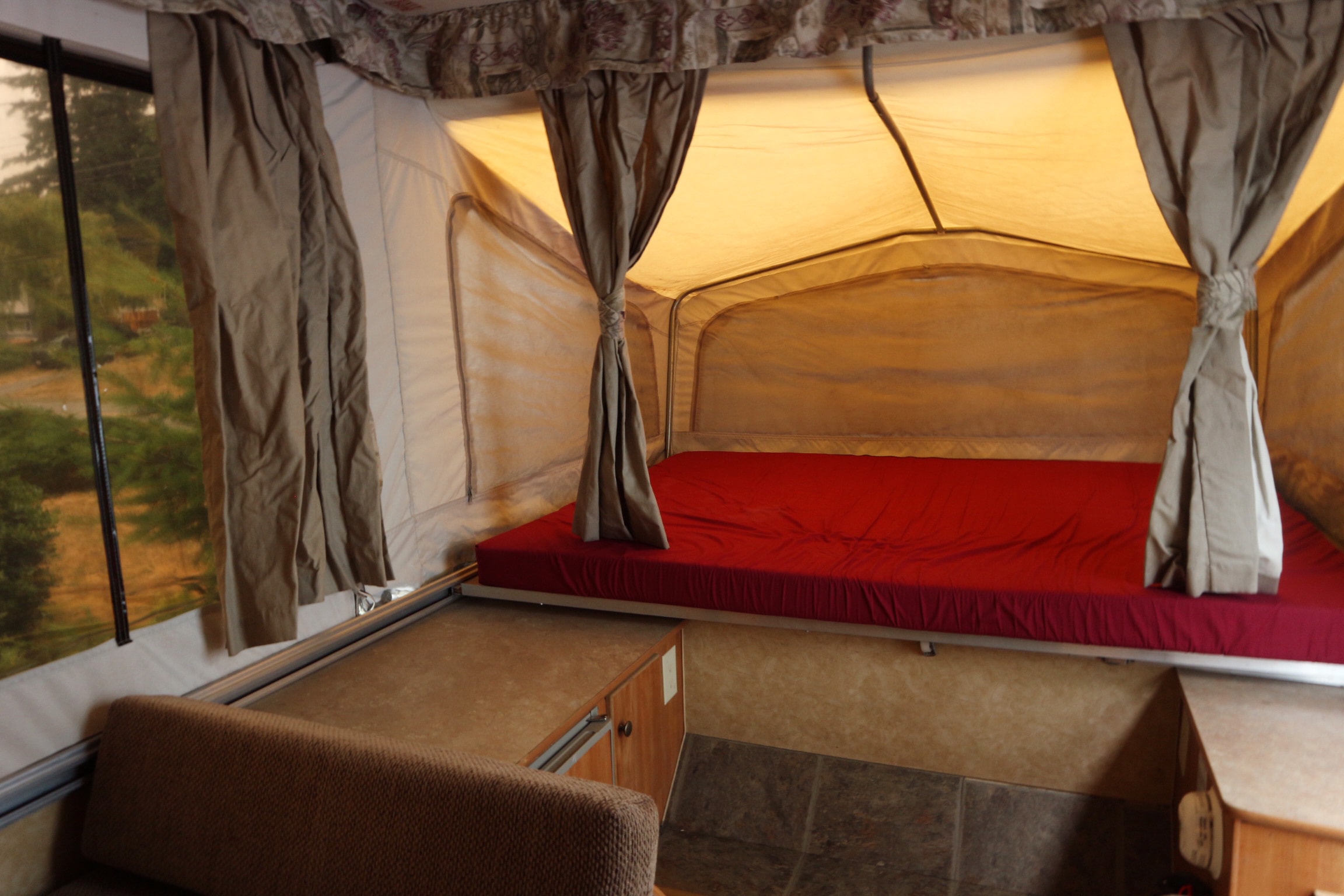 Cozy pop-up RV rental interior: red bed, fabric walls, and a window with green outdoor views.. Starcraft 1701 2006