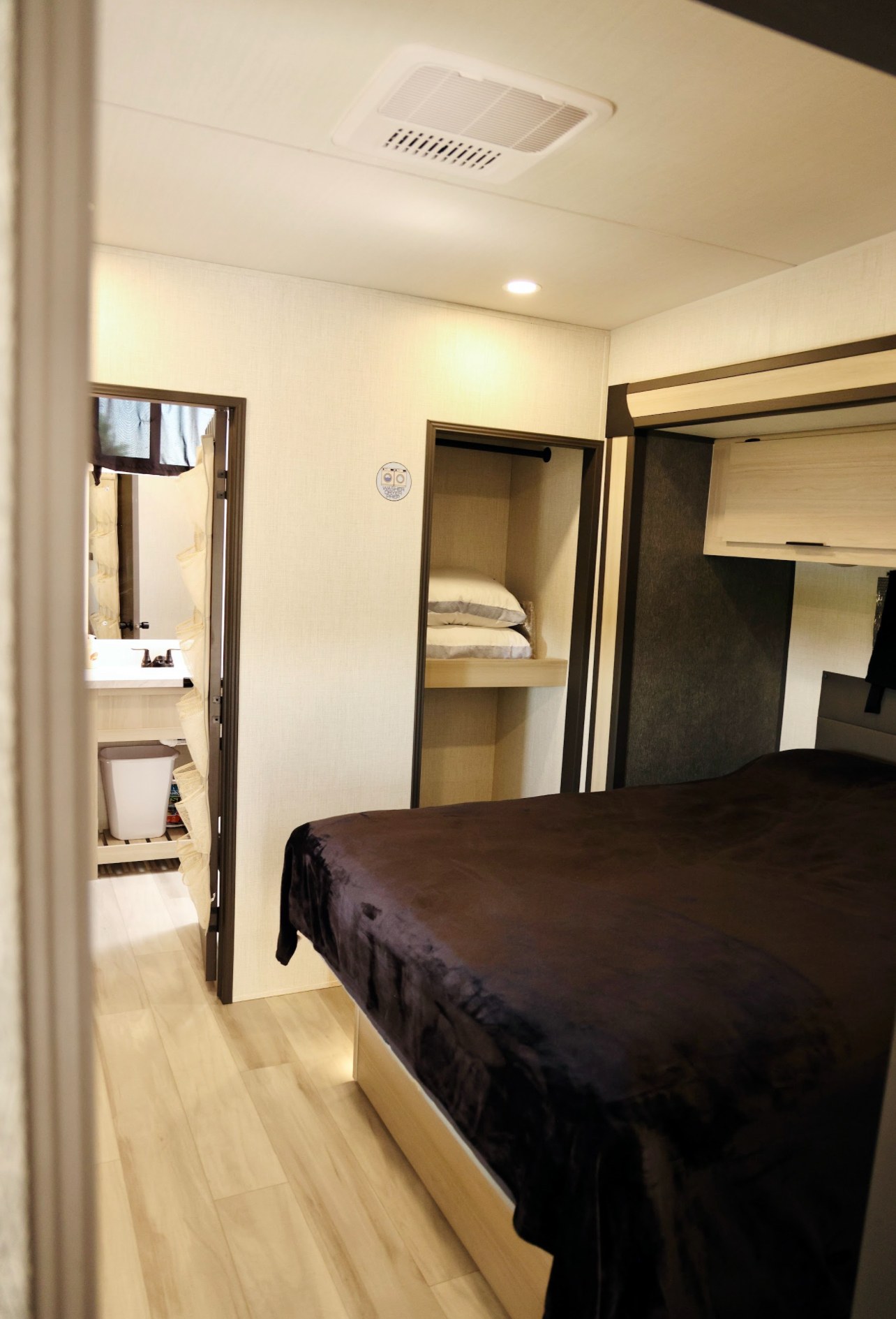 Cozy RV rental bedroom showing a bed, open closet with pillows, and a glimpse into the attached bathroom. Ideal for travel.. Forest River Cardinal 2025