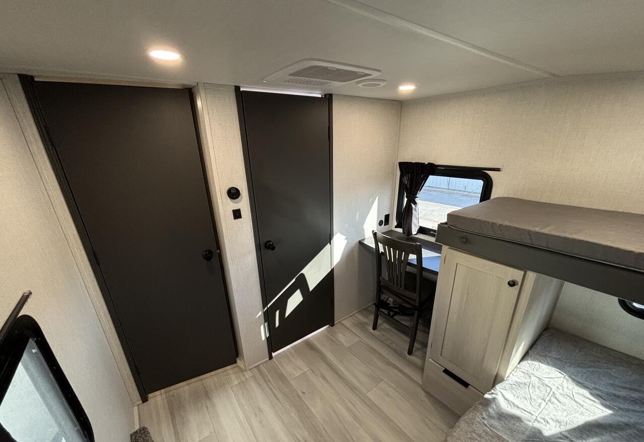 RV rental bunkhouse: light-toned interior with dark doors, a desk, and bunk beds, offering a cozy space.. Forest River Cardinal 2025