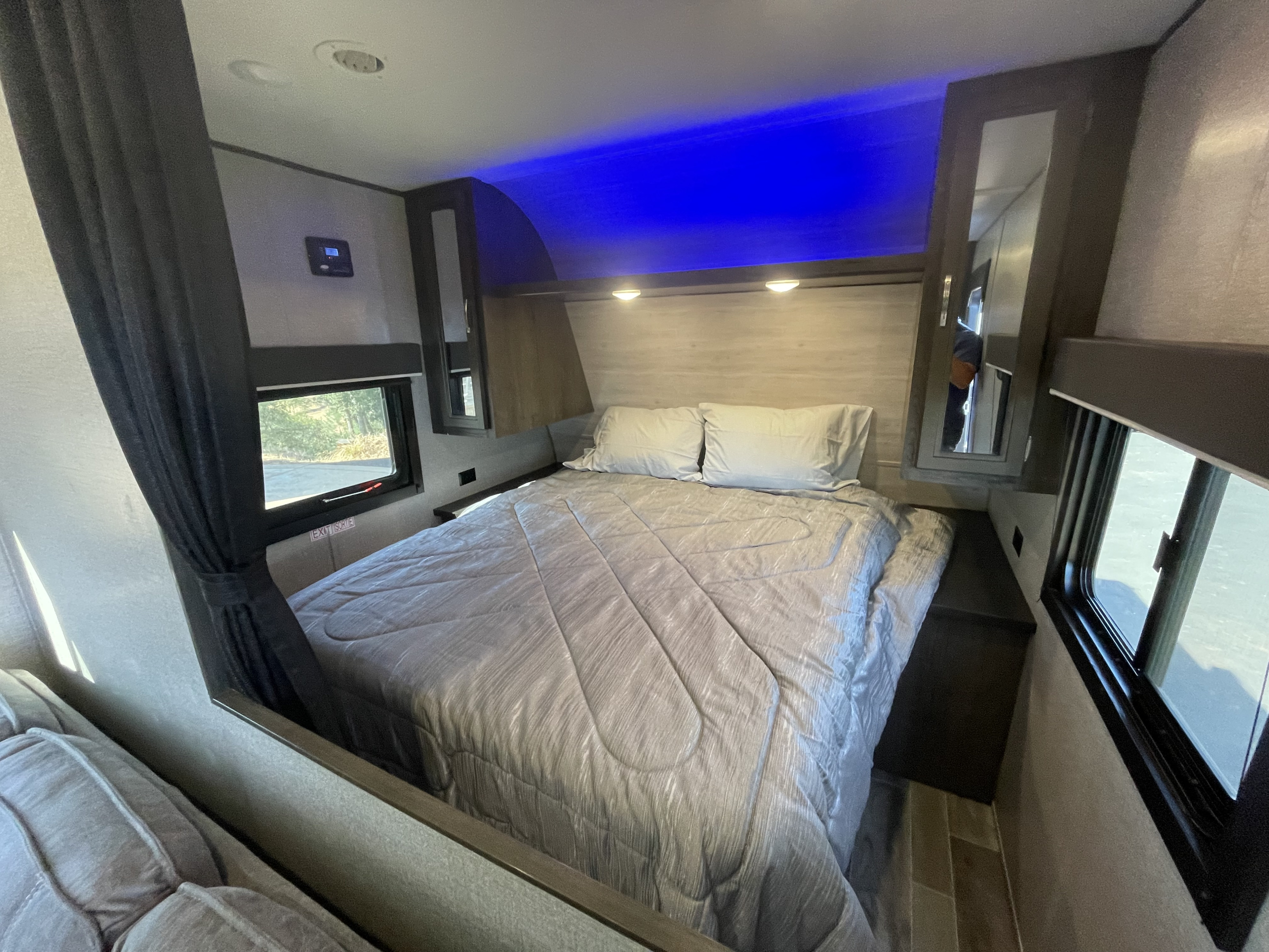 This RV rental bedroom features a comfortable bed, white pillows, blue accent lighting, and windows on both sides.. Jayco Jay Flight SLX Rocky Mountain Edition 2021
