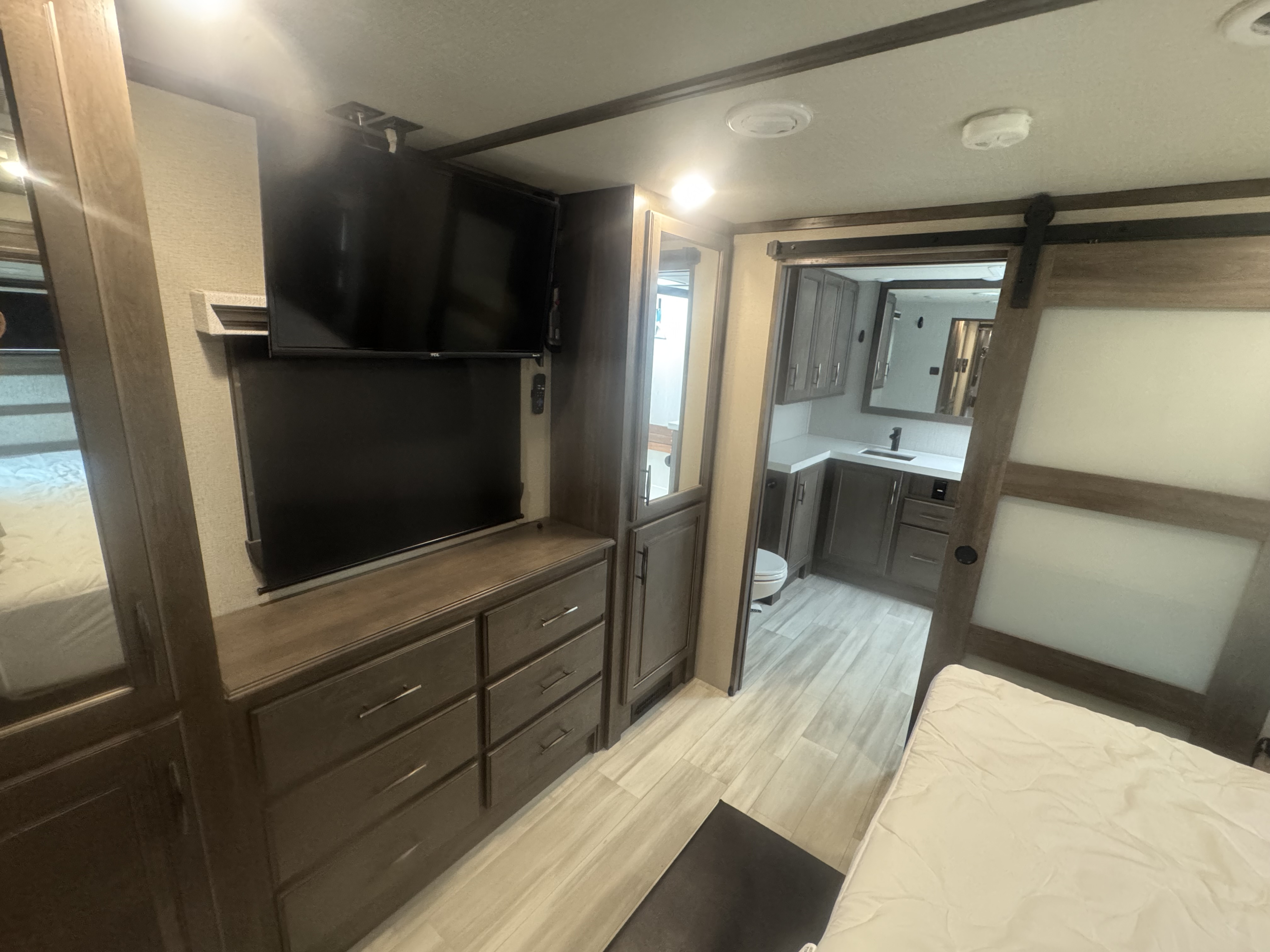 Spacious RV rental bedroom with dresser, dual TVs, and a sliding barn door leading to a modern bathroom.. Grand Design Solitude 2022