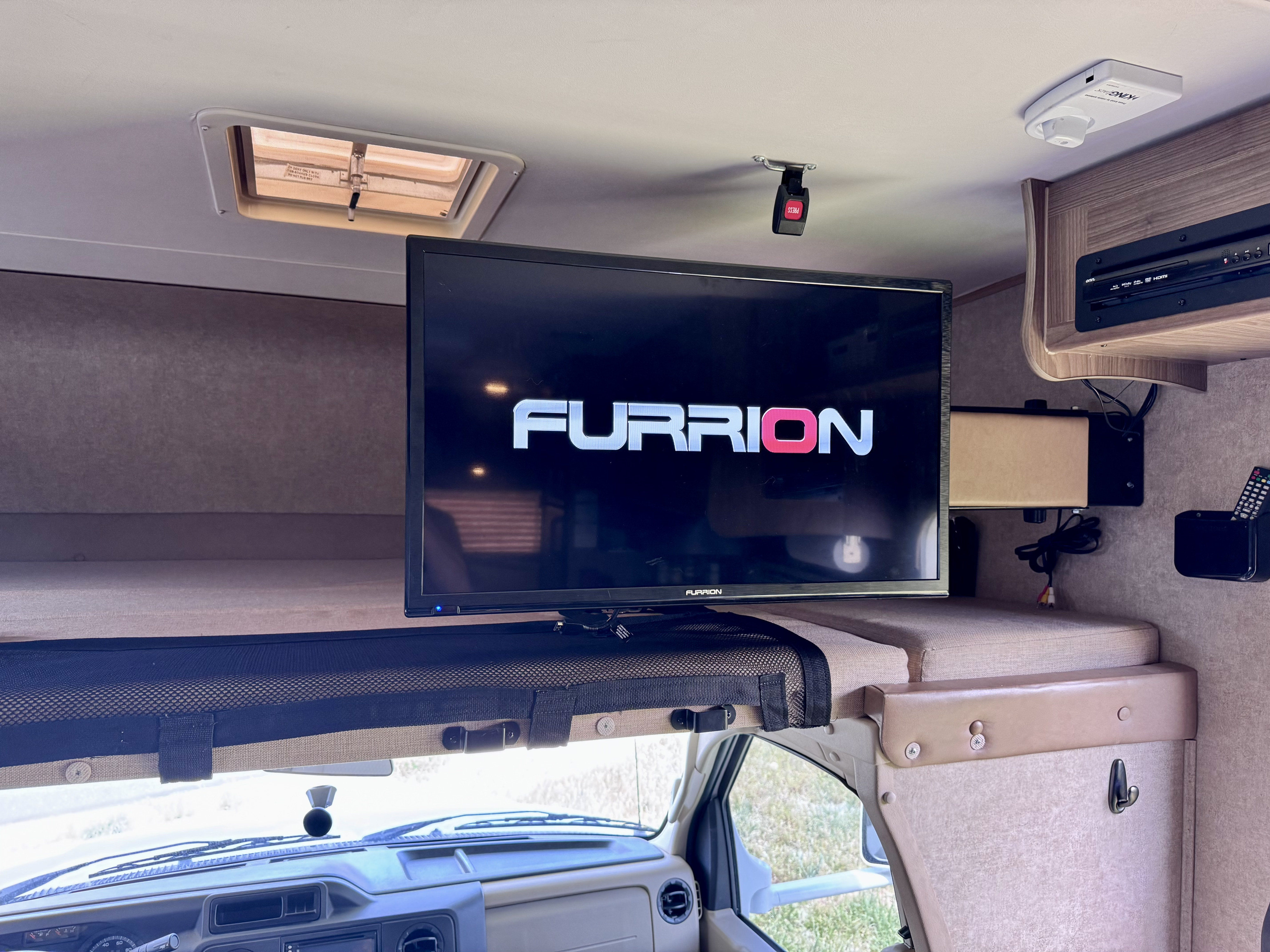 Inside an RV rental: a Furrion TV displays its logo, with a cozy bunk and entertainment system in the overhead cab area.. Coachmen Freelander 21QB 2016