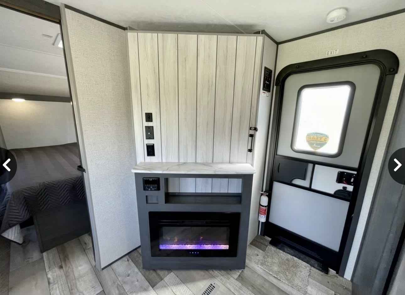 Modern RV rental interior showing a compact living space with an electric fireplace, bedroom entrance, and main entry door.. Aspen Trail Other 2021