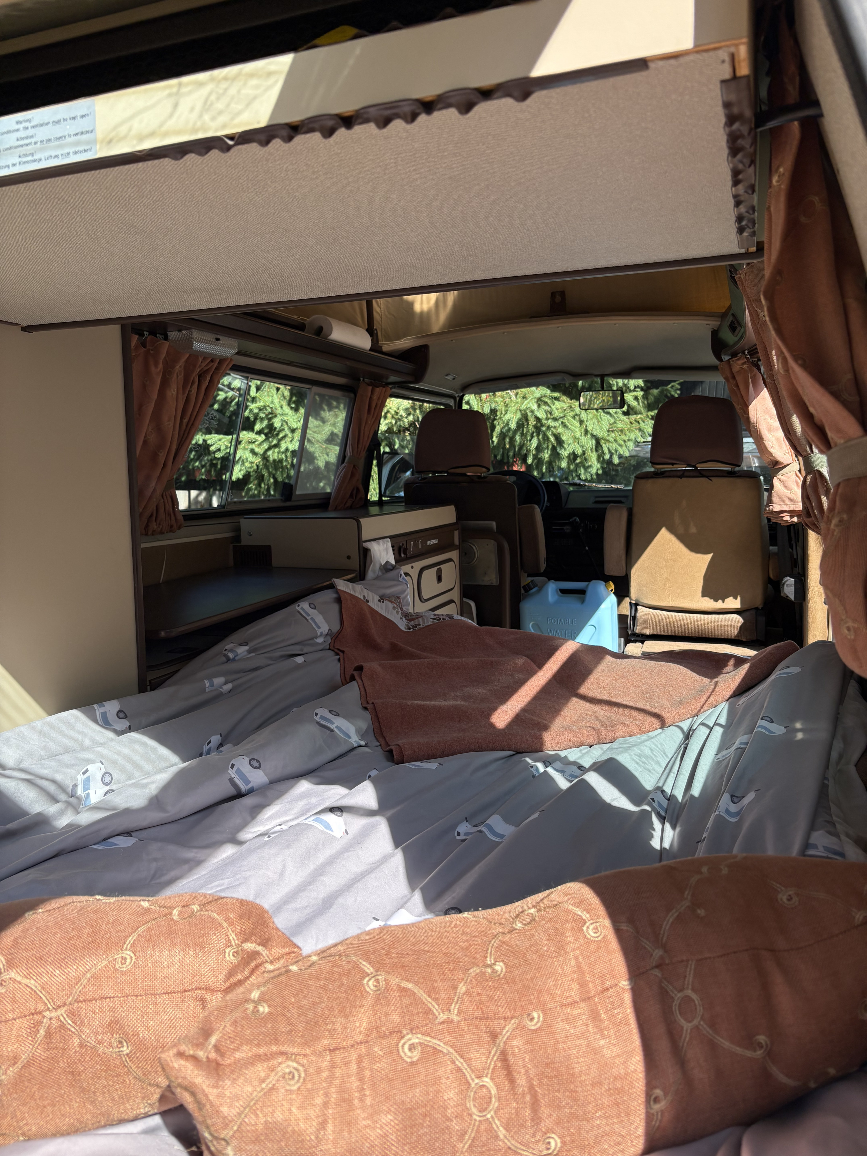 Cozy RV rental interior showing a comfortable bed, compact kitchen unit, and front cab area. Ready for road trips!. Westfalia T3 Westfalia 1986