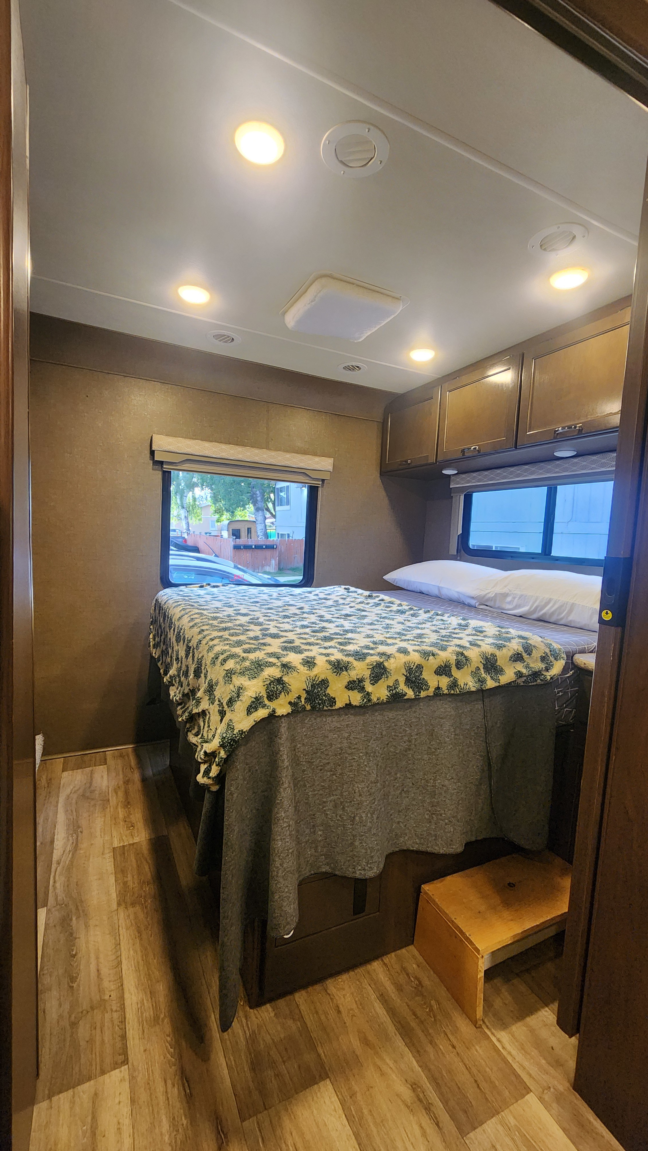 Cozy RV rental bedroom featuring a comfortable bed, windows, overhead storage, and a wooden step stool.. Thor Freedom Elite 2018